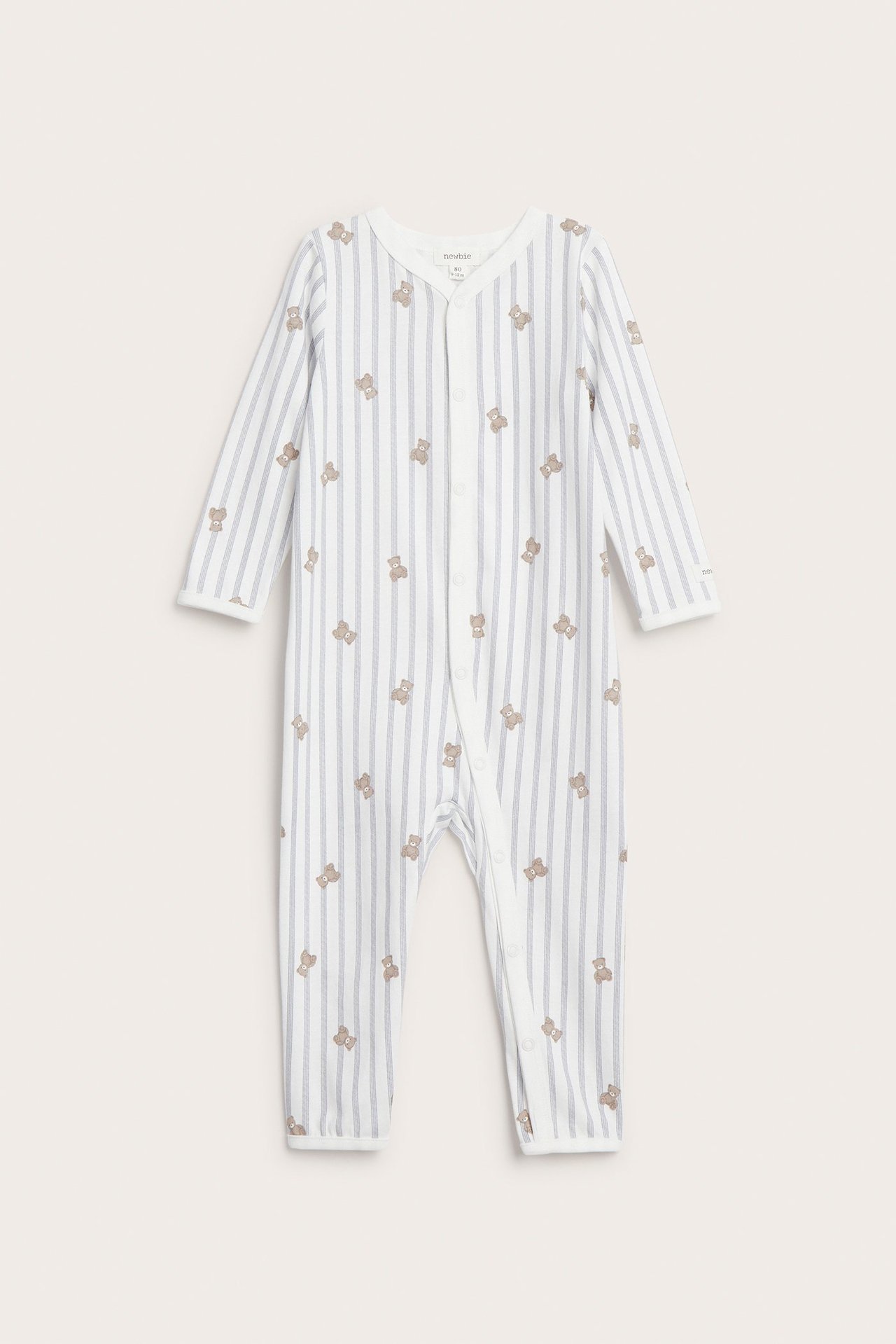 Edestä näkymä vauvan luonnonvalkoisesta raidallisesta puuvillapyjamasta nallekuviolla ja painonapeilla.