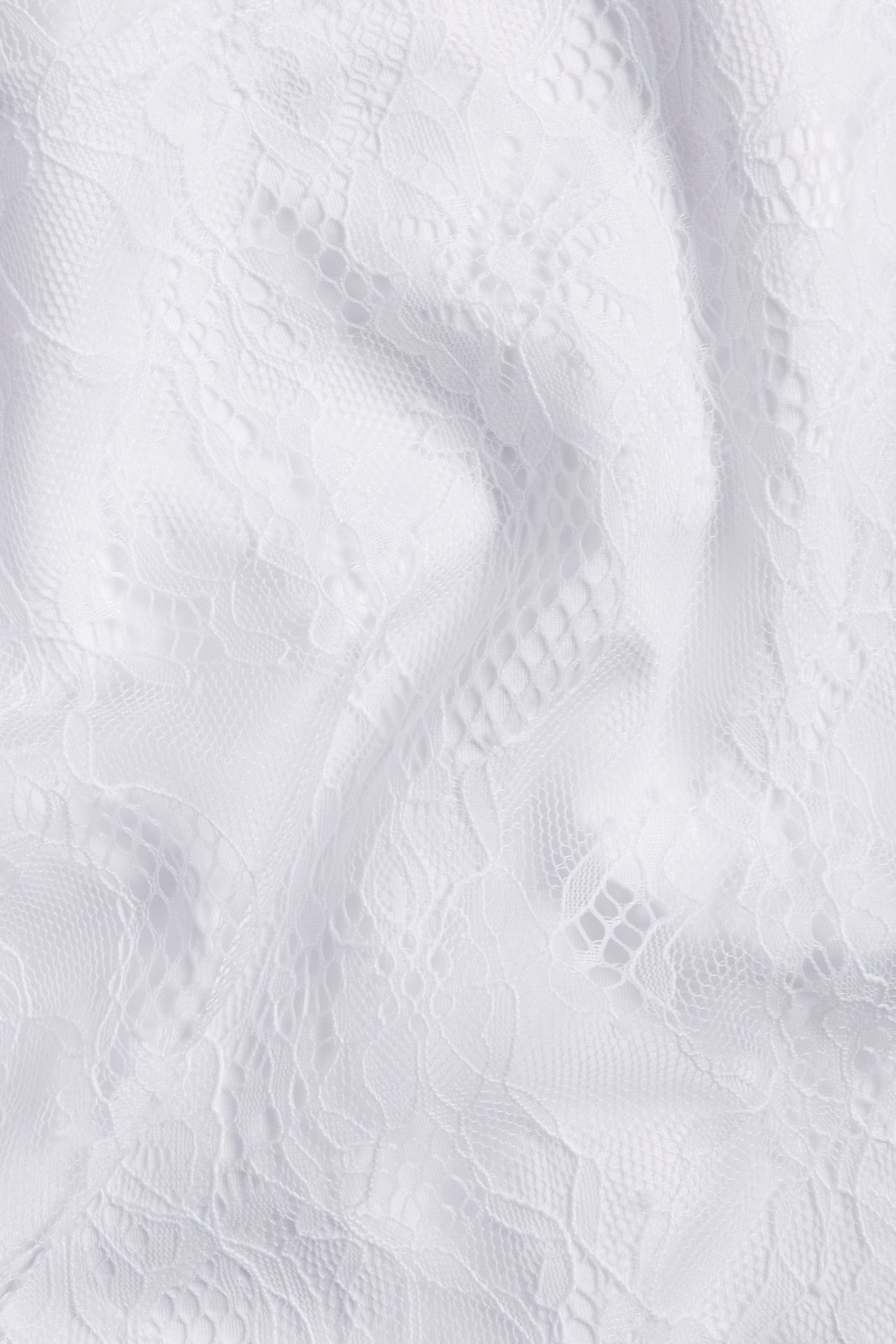 Zbliżenie białej tkaniny sukienki z koronki, z detalicznym kwiatowym wzorem i miękkimi fałdami.