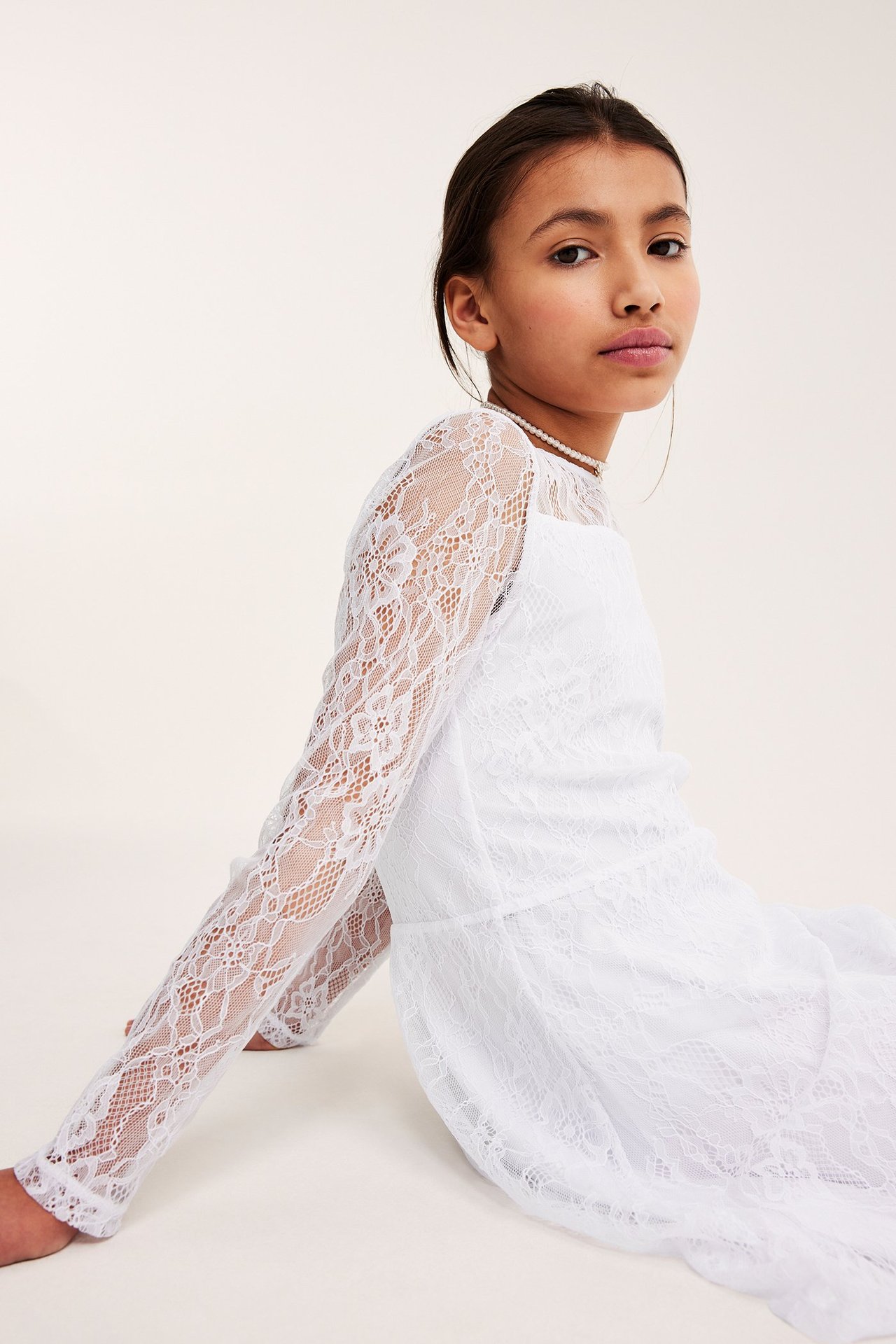 Hvit blondekjole i poly jersey og blonde, jente sitter på gulvet, frontvisning.