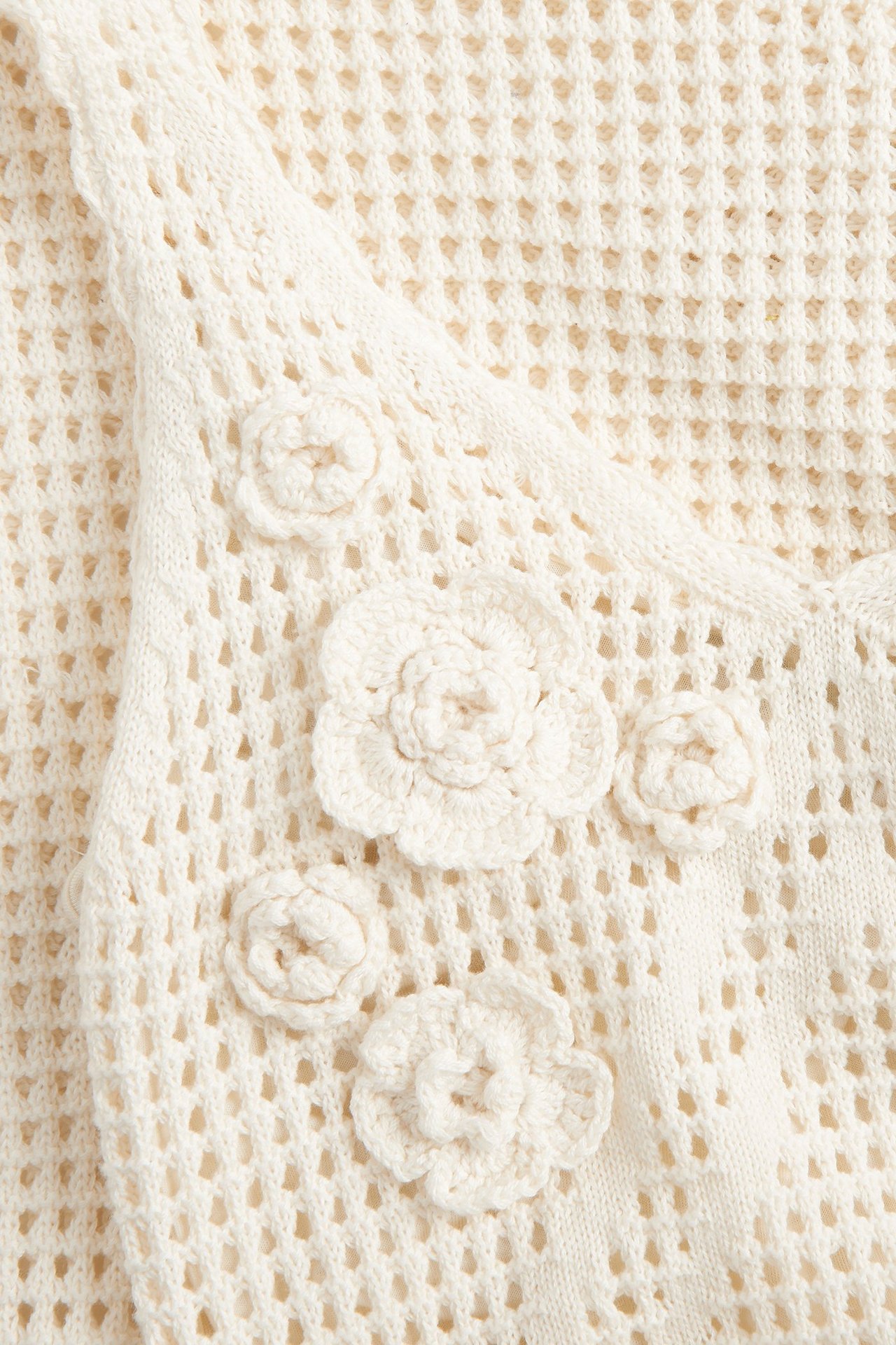 Zbliżenie beżowej, ażurowej sukienki szydełkowej z kilkoma aplikacjami szydełkowych kwiatów.