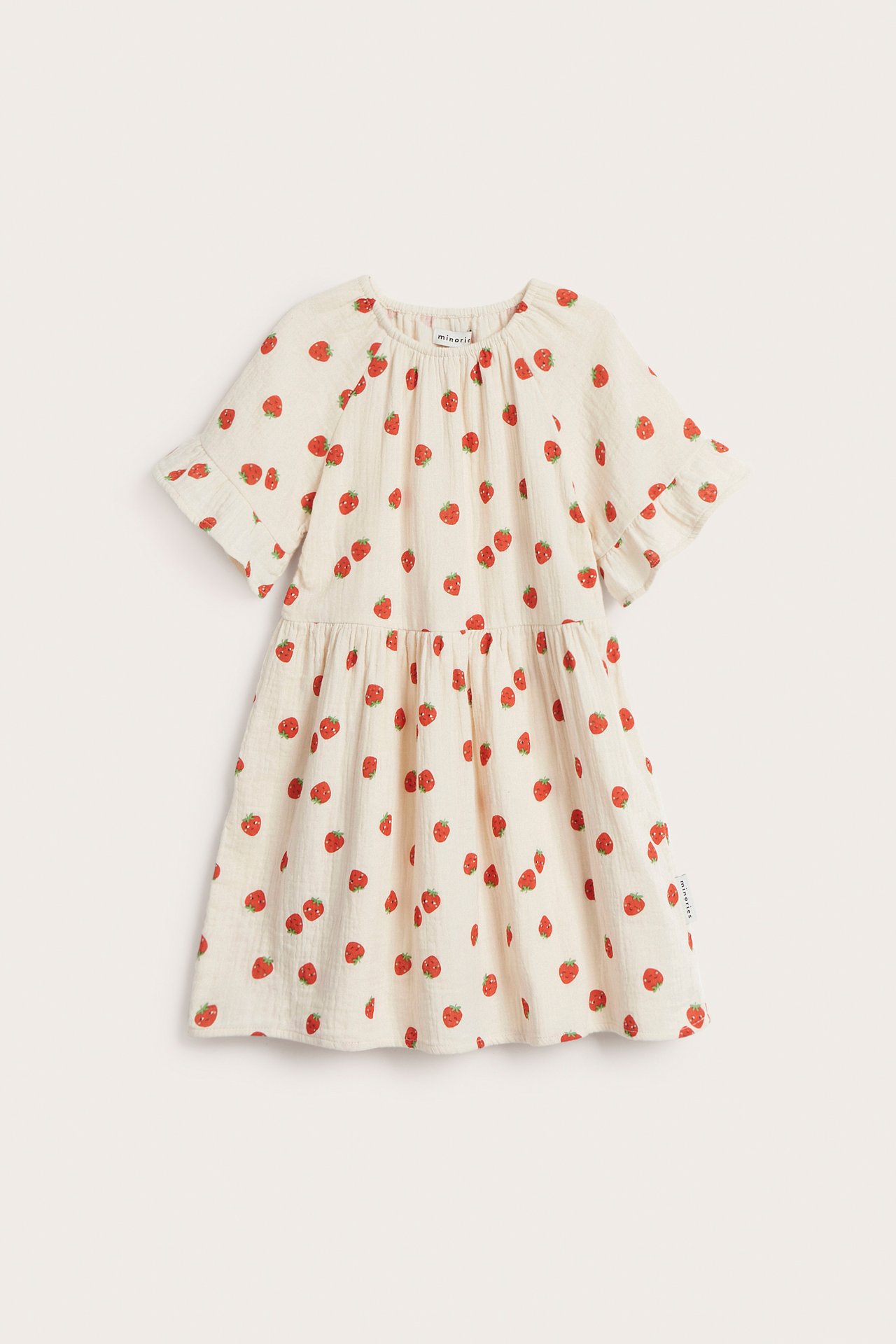 Framsida av en barnklänning i off-white muslin med korta ärmar, rött jordgubbsmönster och volangärmar.