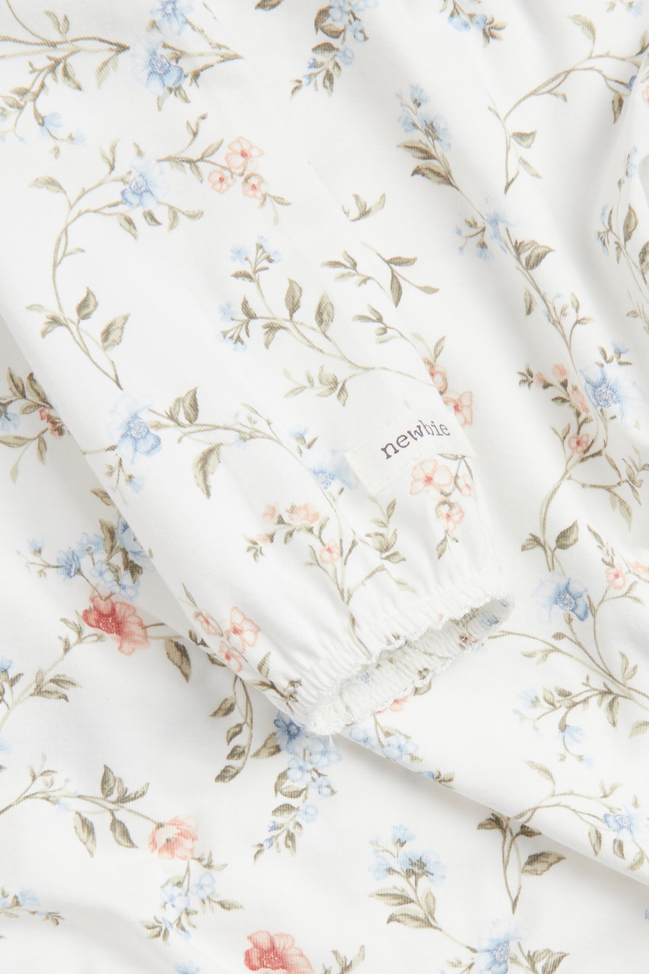 Närbild på en offwhite babybody med långa puffärmar, blommigt mönster och resår i ärmslut.