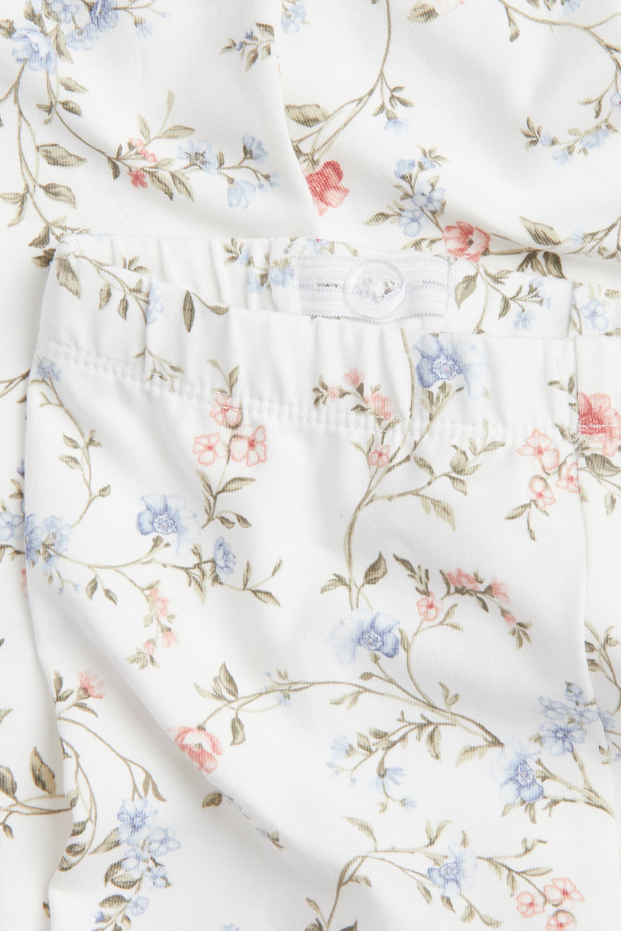 Närbild av offwhite blommiga leggings med rosa och blå blommor, med justerbar resår i midjan och knapp.