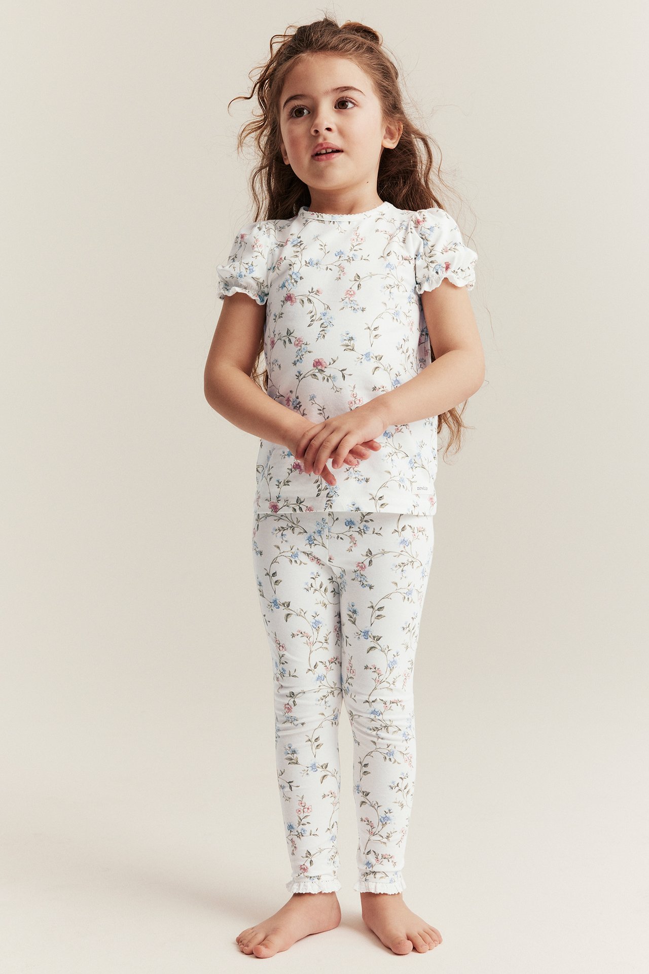 Frontvy av ett barn i offwhite blommiga leggings med spets och en matchande kortärmad topp.