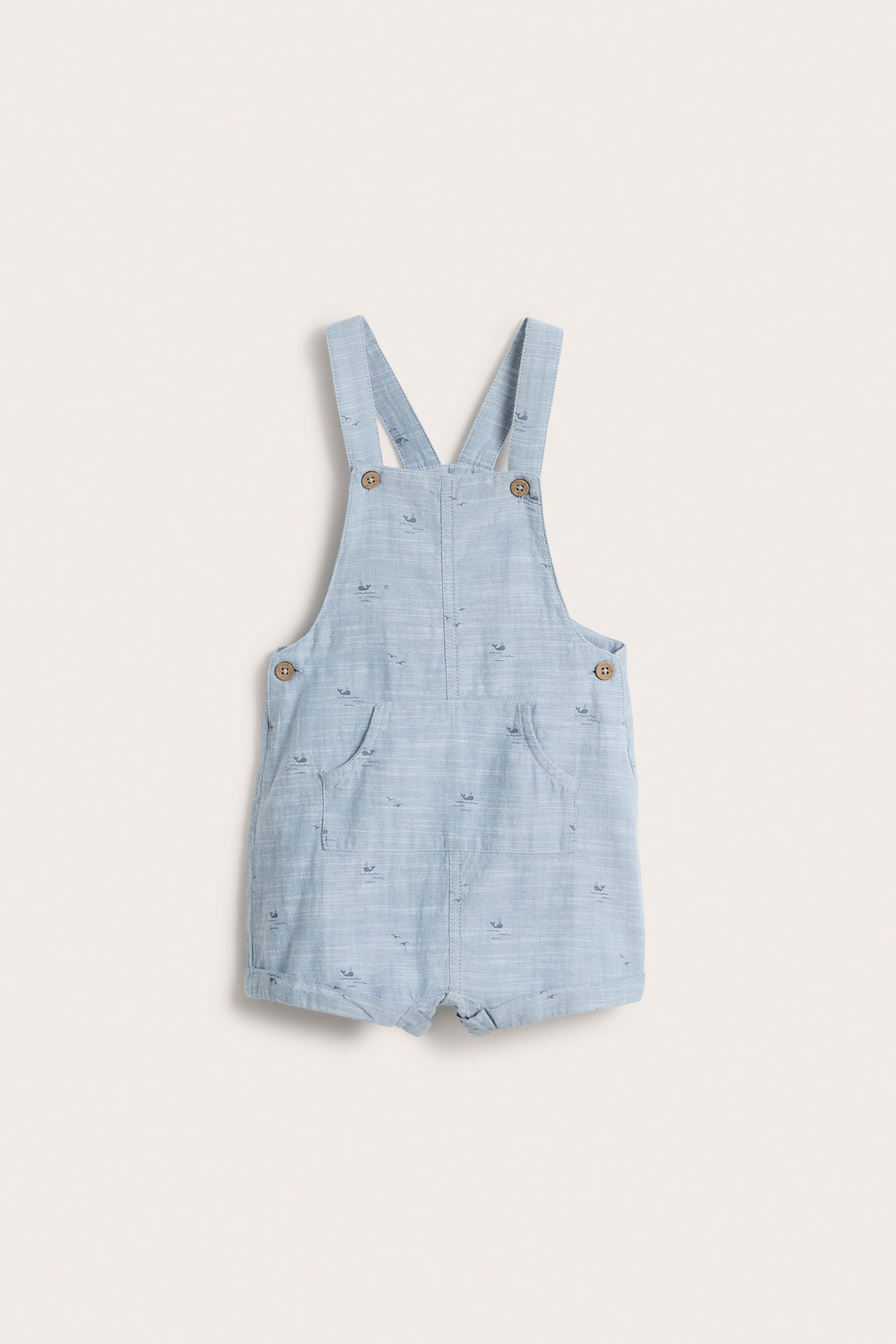 Edestä kuvattu vaaleansininen chambray-vauvanhaalarishorts, jossa on hienovarainen eläinkuvio, säädettävät olkaimet ja etutasku.