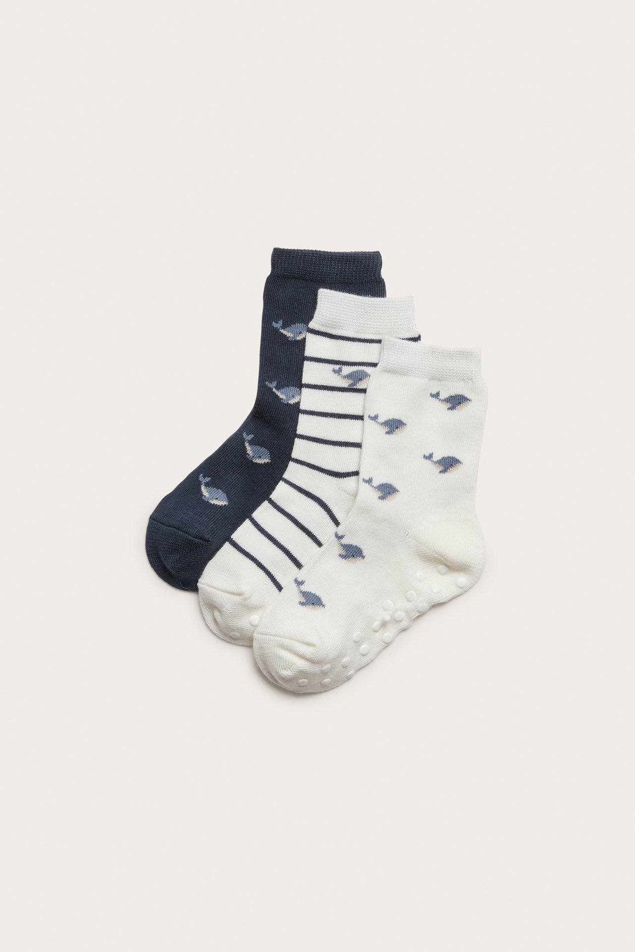 Frontvy: Tre par barnstrumpor. Off-white valmönstrade med antislip, randiga och mörkblå.
