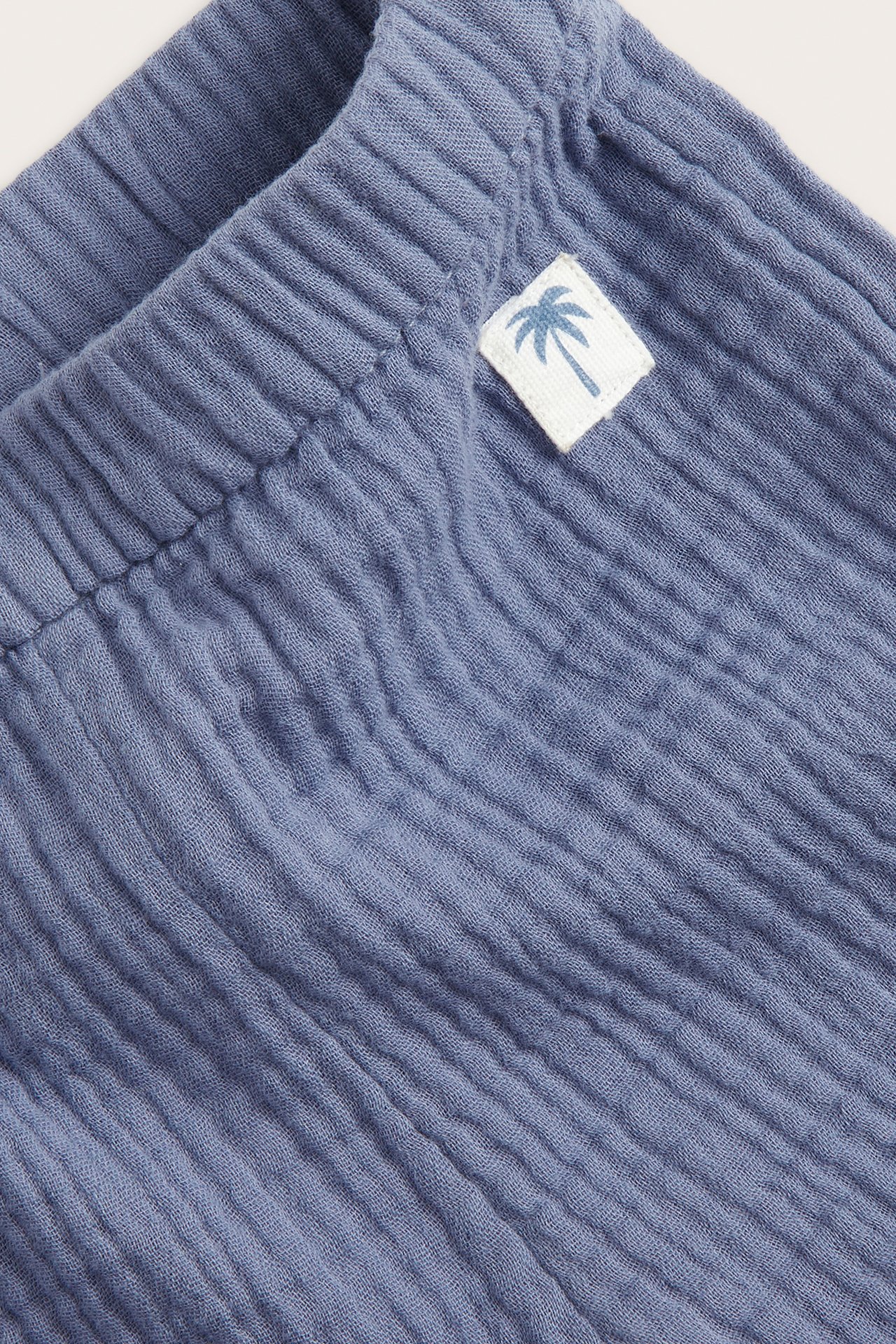 Närbild av blå muslin baby shorts med resår i midjan och en liten palm-etikett.
