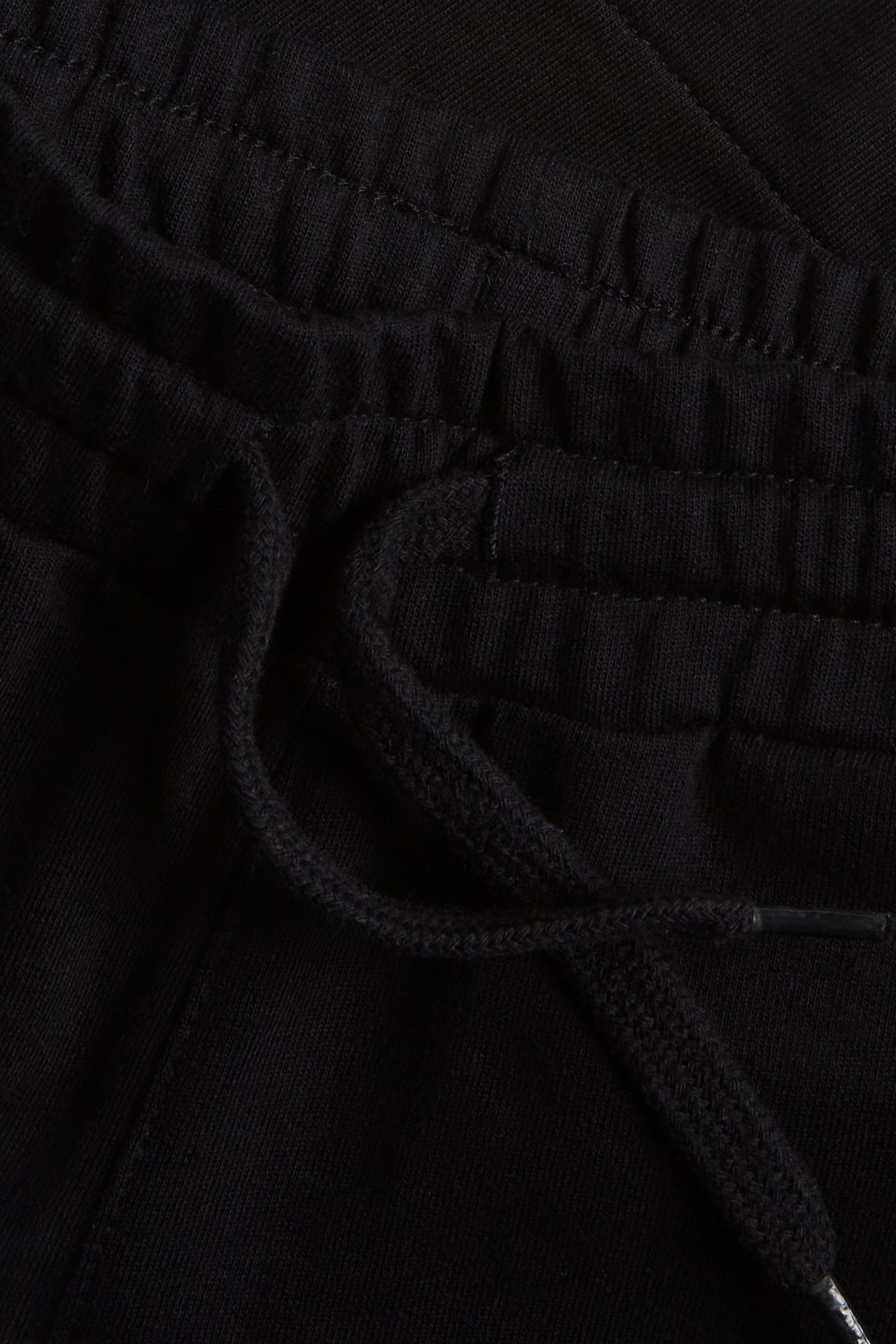 Zbliżenie na czarne bawełniane szorty dresowe z elastycznym pasem i sznurkiem.