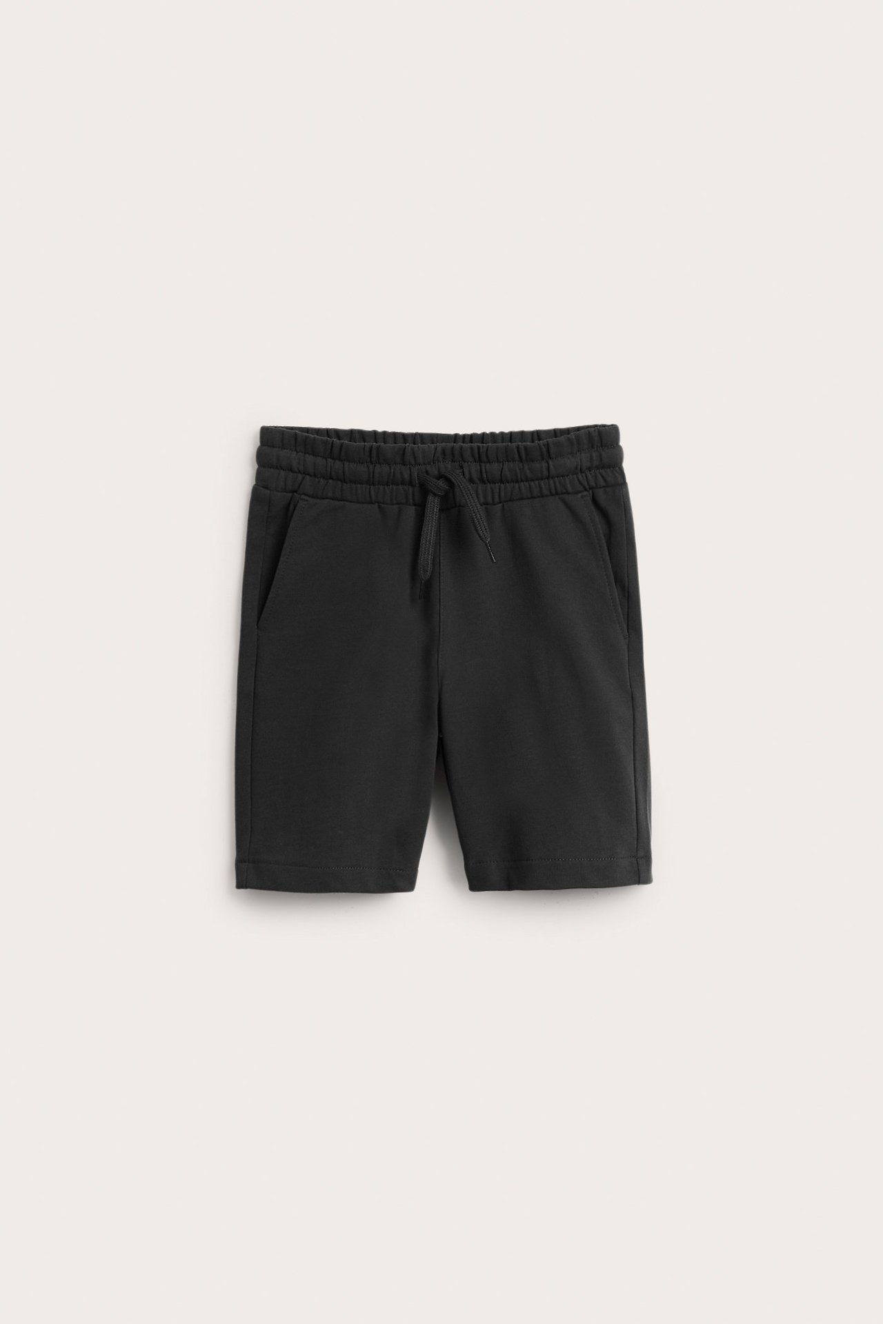 Frontvy av svarta bomullsshorts för barn med elastisk dragsko i midjan och sidfickor.