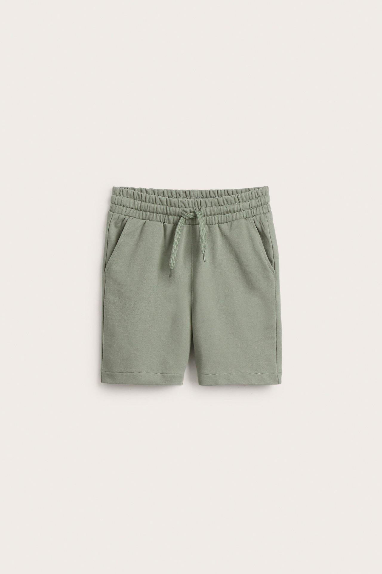 Frontvy av mörkgröna mjukisshorts i bomull för barn med resår och dragsko i midjan.