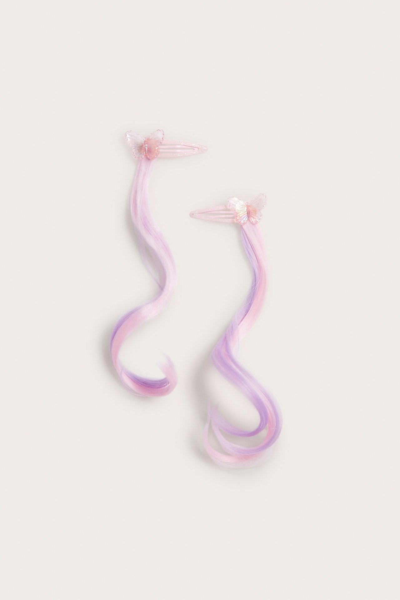 Ylhäältä kuvattuna kaksi vaaleanpunaista hiusklipsiä glitterperhosilla ja pitkällä aaltoilevalla vaaleanpunaisella ja violetilla tekohiuksella.