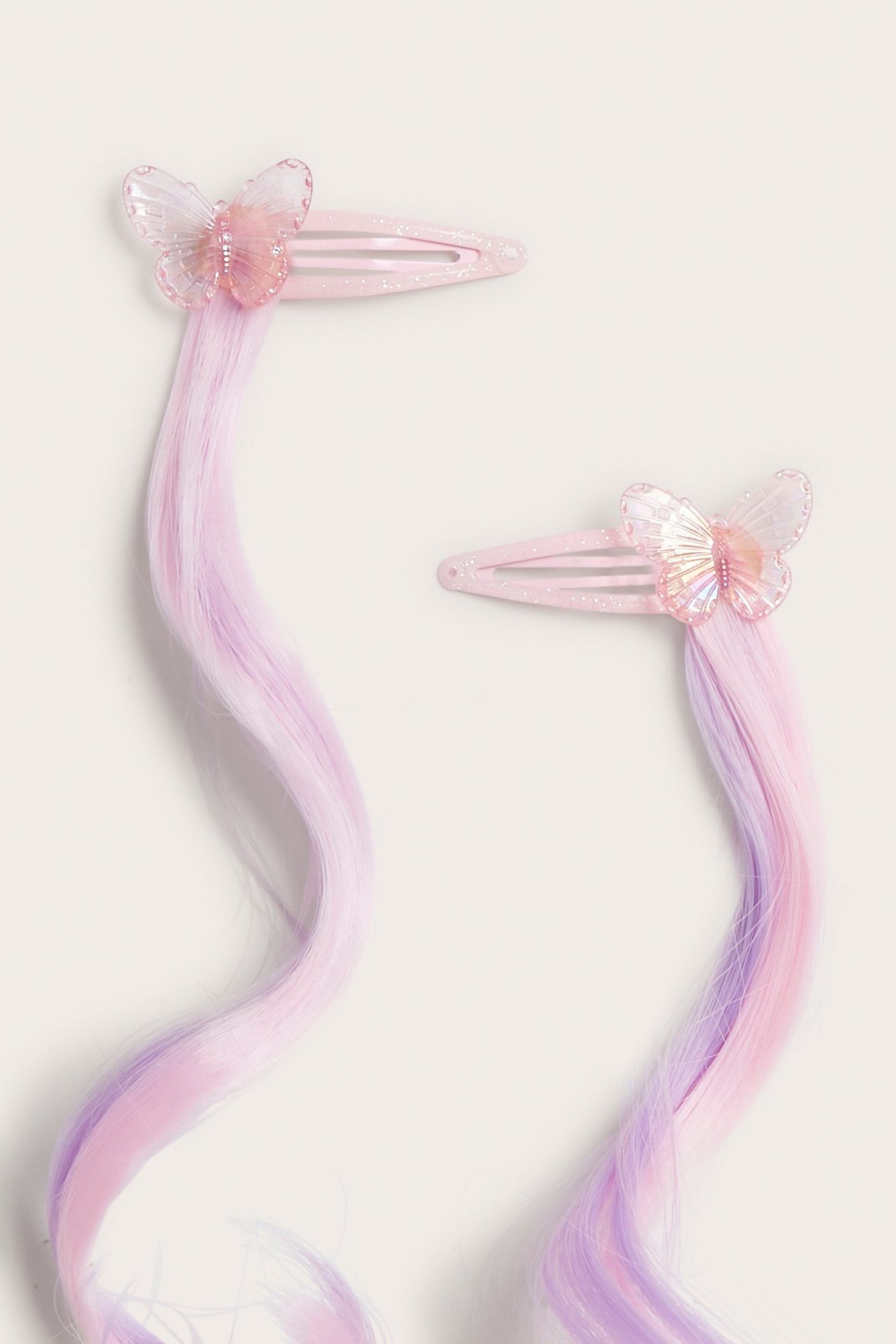 Lähikuva kahdesta vaaleanpunaisesta glitterhiusklipsistä, joissa on hohtavat perhoset ja pitkät pinkki-violetit tekohiukset.