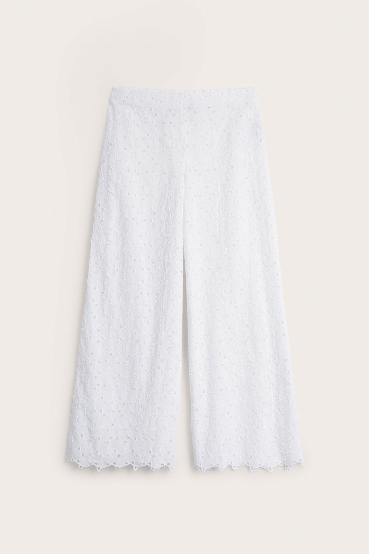 Edestä näkymä valkoisista leveälahkeisista puuvillapitseistä housuista, joissa on aaltoileva helma ja sivuvetoketju.