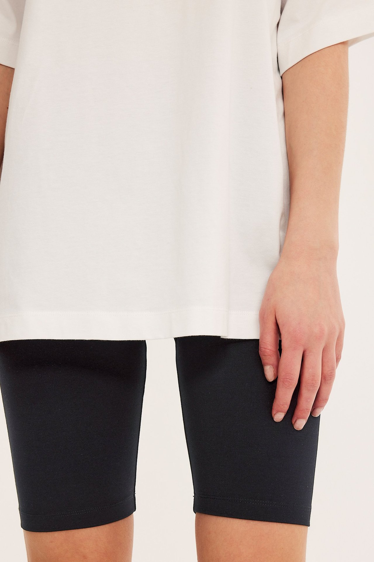 Forfra, kvinne i svarte trikot-sykkelshorts under en løs hvit t-skjorte.