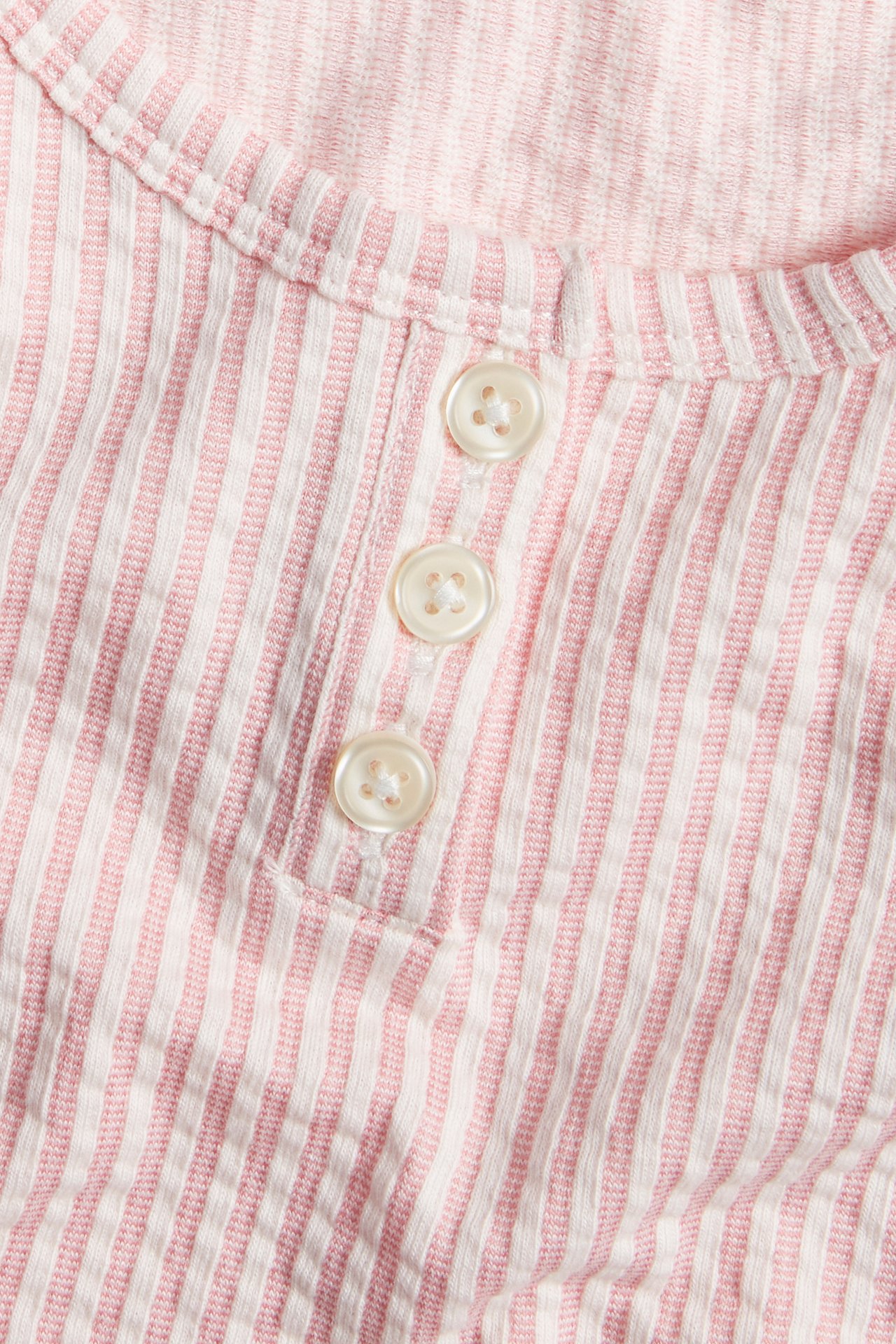 Nærbilde av en rosa og hvitstripet pyjamastopp med seersucker-struktur og tre hvite knapper.