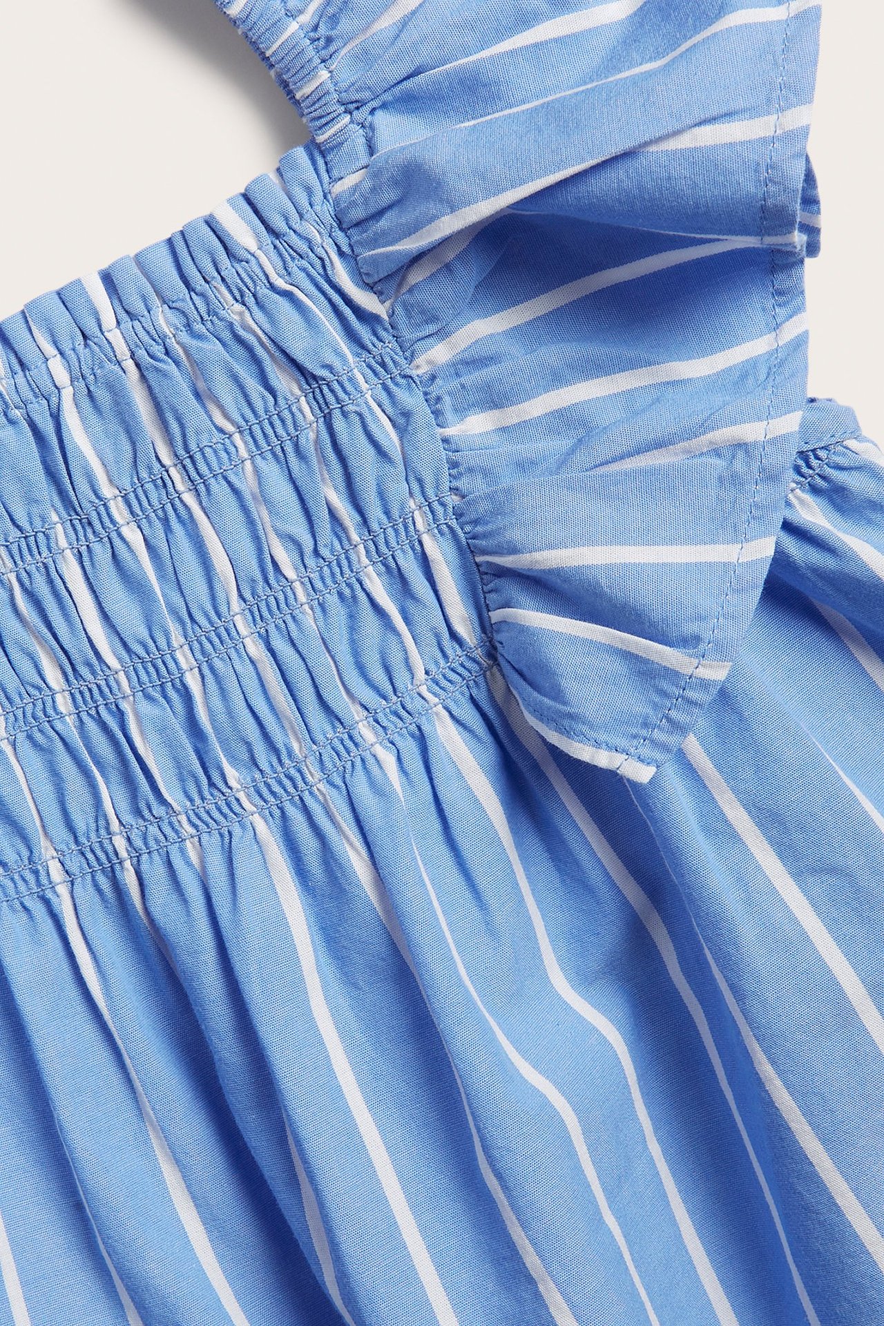 Zbliżenie na niebiesko-biały bawełniany top w paski z falbankami i marszczeniem.