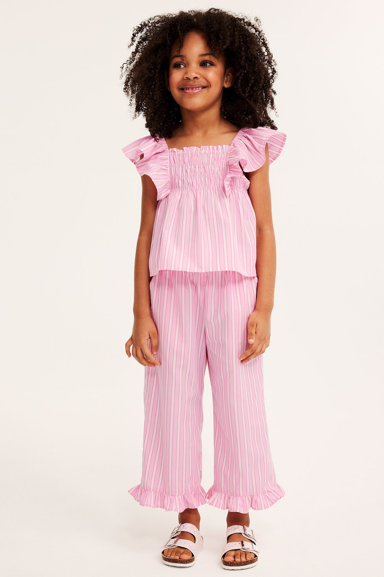 Widok z przodu: Dziecko w różowo-białych spodniach culotte w paski, pasującym topie i różowych sandałach.