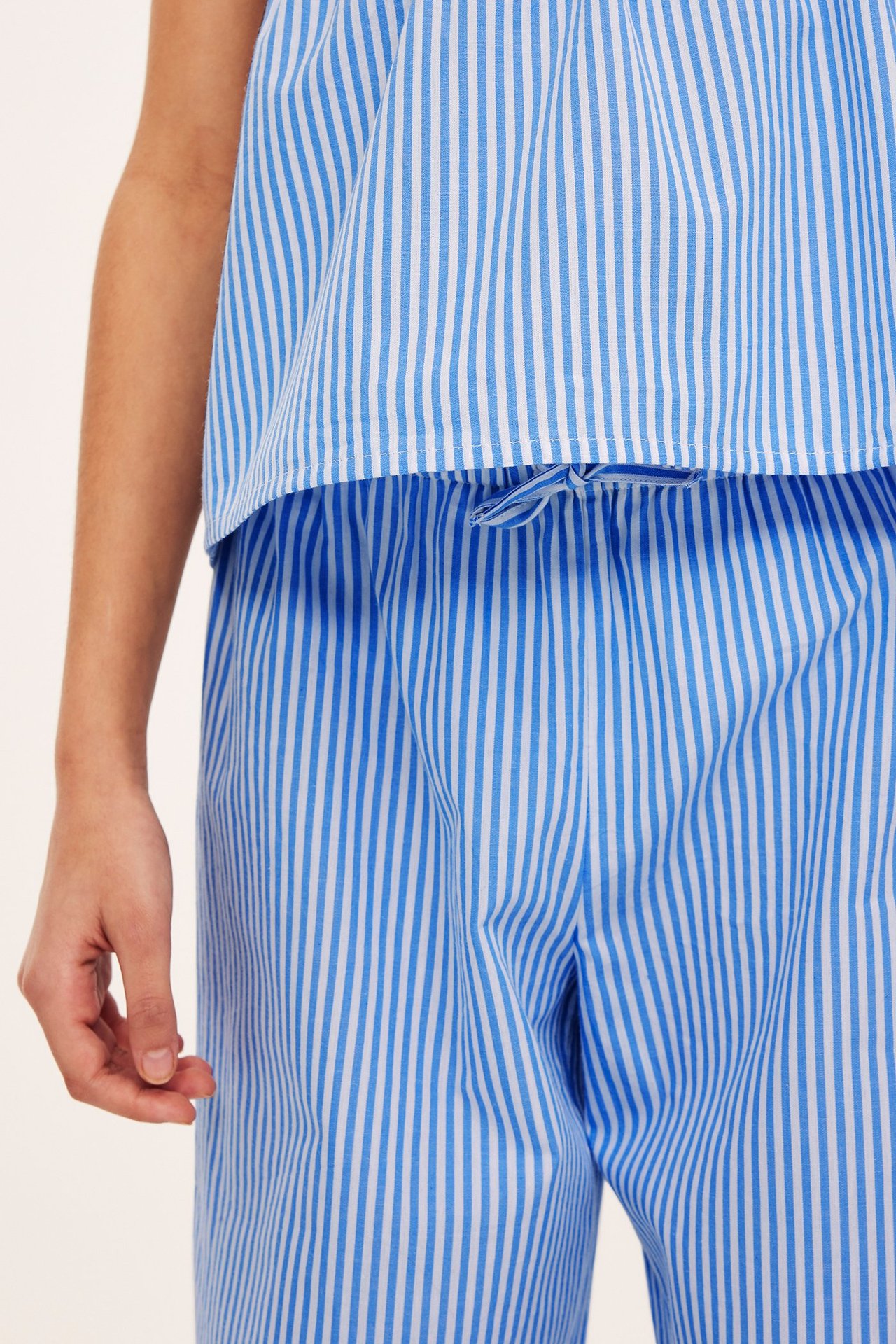 Närbild på ett barn i blåvitrandiga bomullsbyxor med dragsko i midjan och matchande topp.