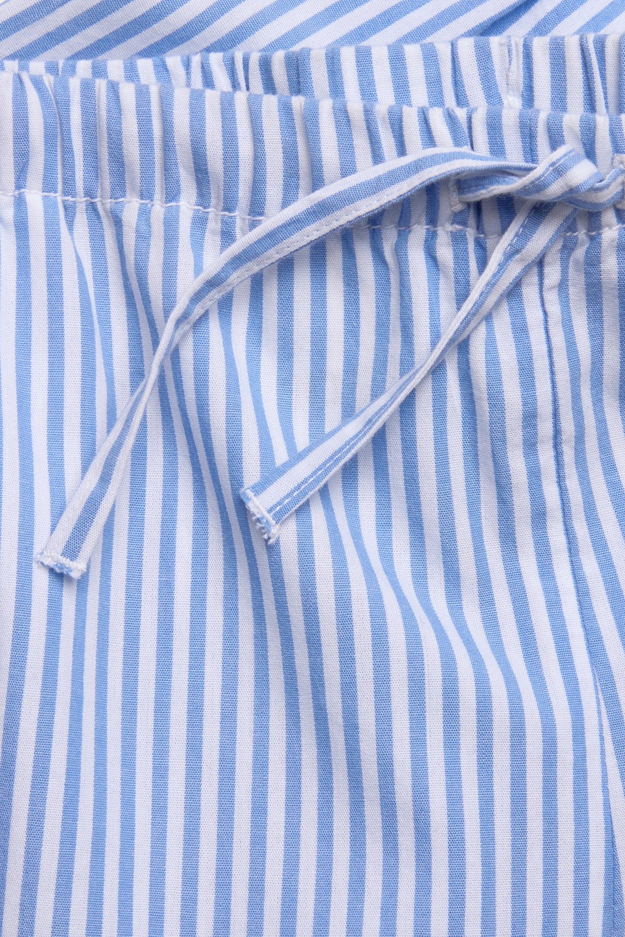Zbliżenie na niebiesko-białe bawełniane szorty w paski z elastyczną talią i wiązaniem.