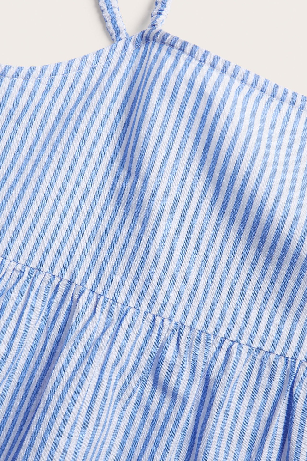 Zbliżenie na niebiesko-biały, pasiasty top z teksturowanej bawełny z cienkimi ramiączkami i marszczeniami.