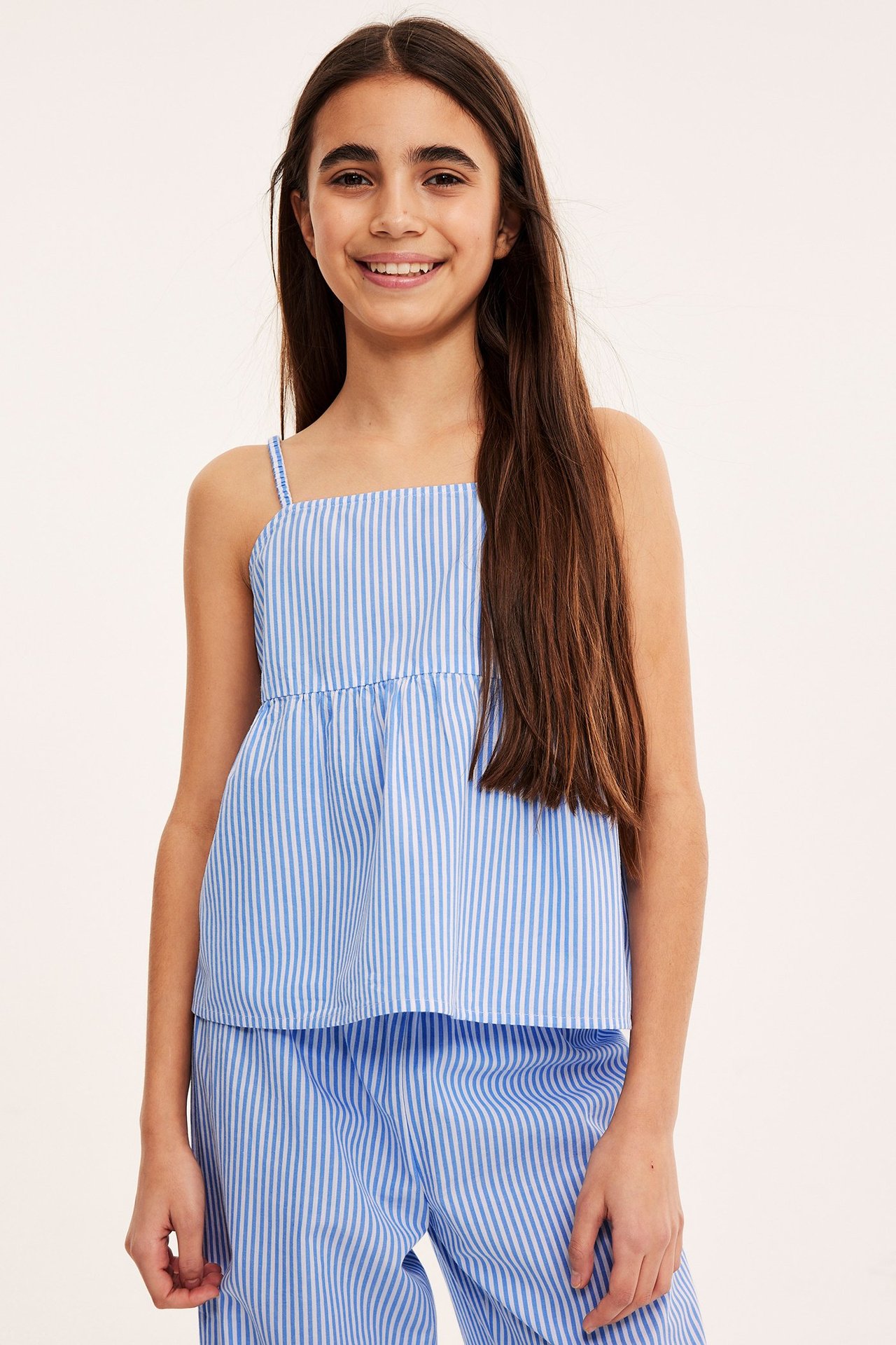 Framifrån på ett barn i en blåvitrandig bomullstopp med smala axelband och matchande randiga byxor.