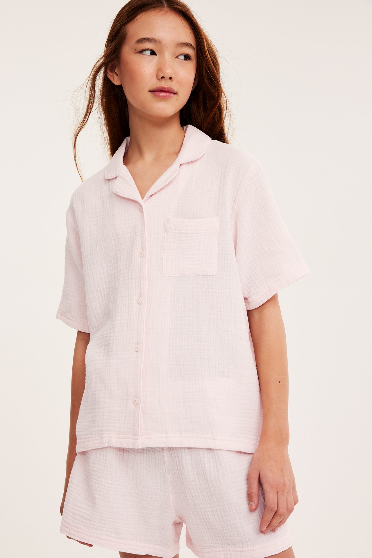 Edestäpäin, lapsi yllään vaaleanpunainen musliininen lyhythihainen pyjamapaita ja yhteensopivat shortsit.