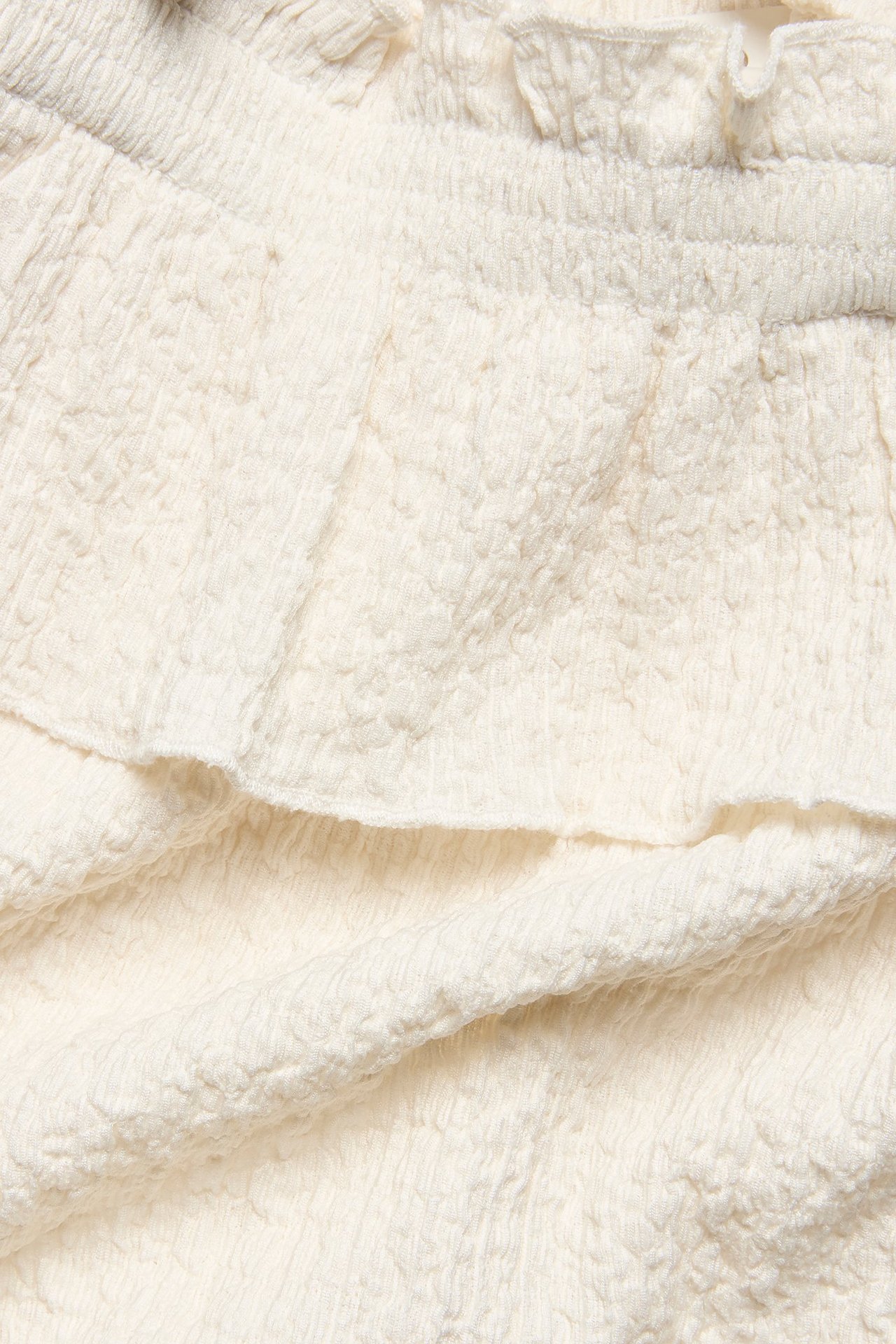 Zbliżenie na kremowy, teksturowany top dziecięcy ze smockiem i ozdobnymi kokardkami.