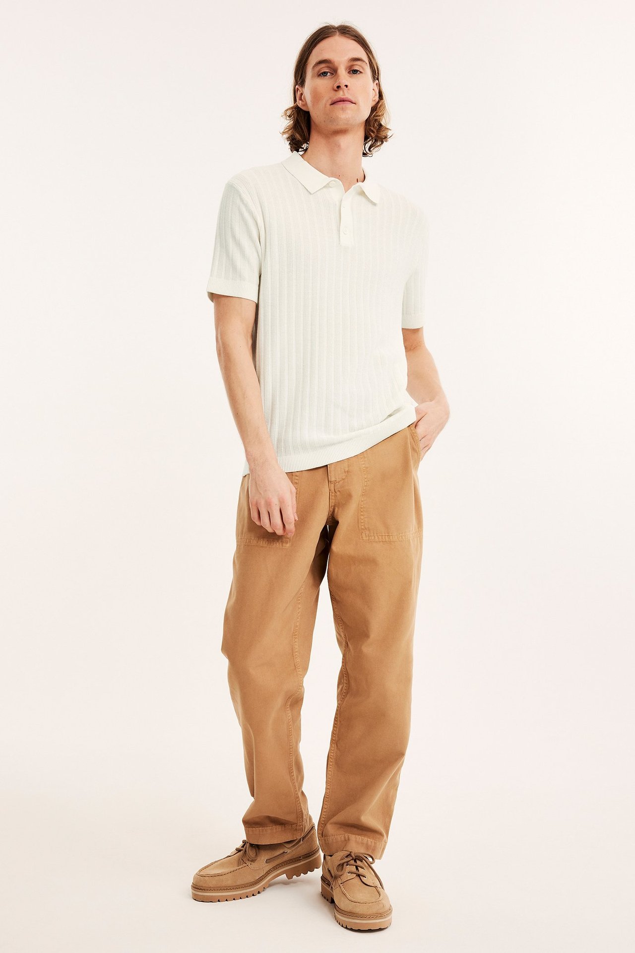 Edestä: mies yllään luonnonvalkoinen hienoneulottu ribattu pikeepaita, beiget cargohousut ja beiget purjehduskengät.