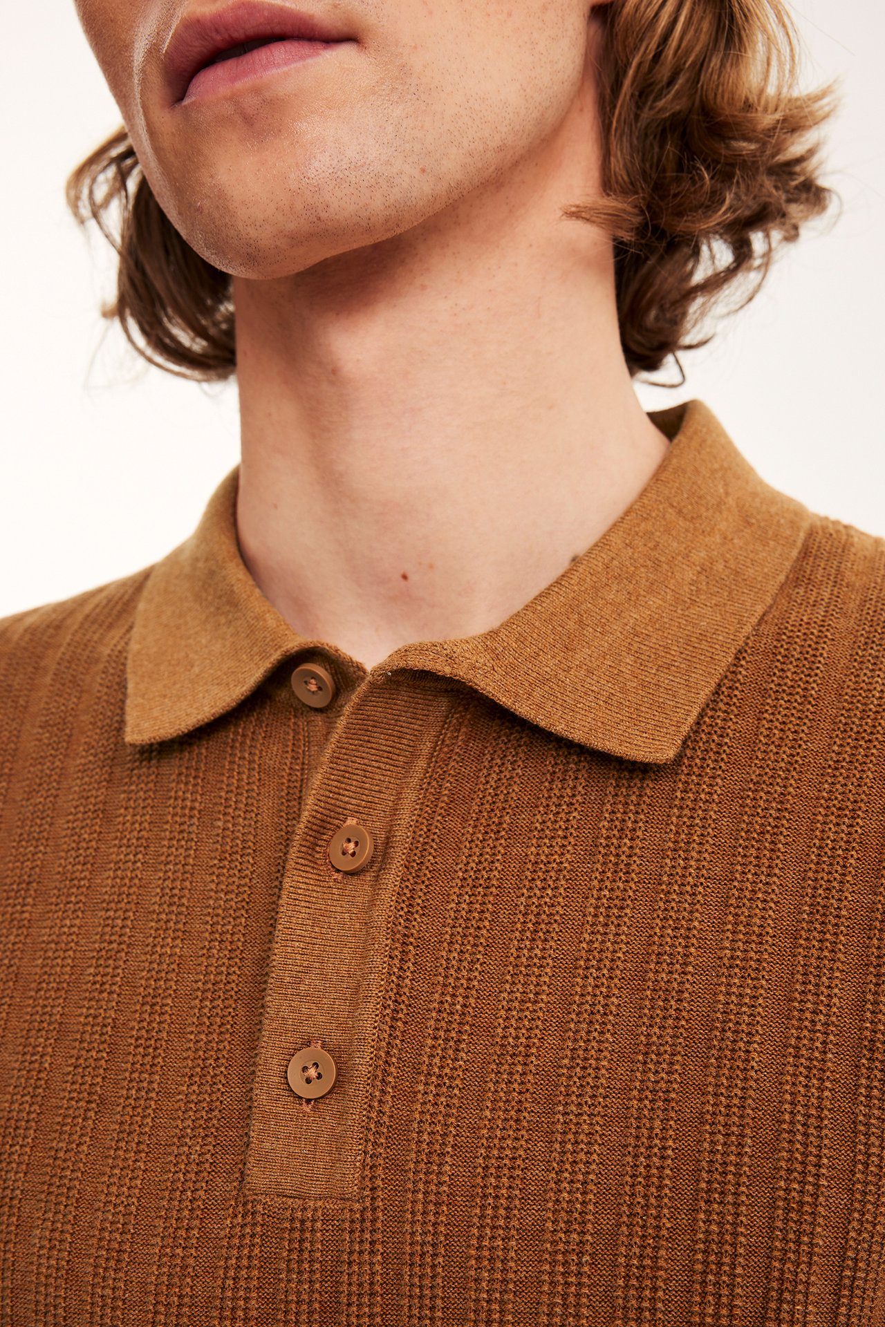 Zbliżenie z przodu: mężczyzna w brązowej, prążkowanej koszulce polo z kołnierzykiem i trzema guzikami.