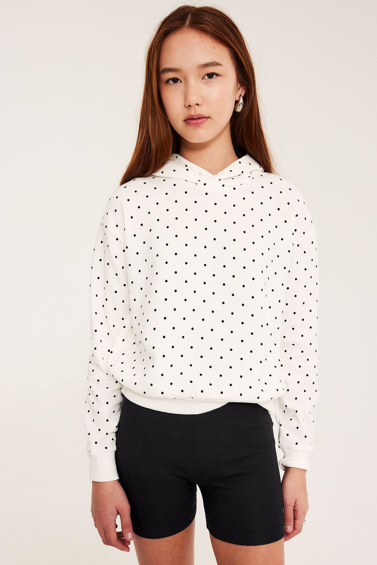 Edestäpäin: lapsi mustissa ribatuissa pyöräilyshortseissa ja valkoisessa pilkullisessa hupparissa.