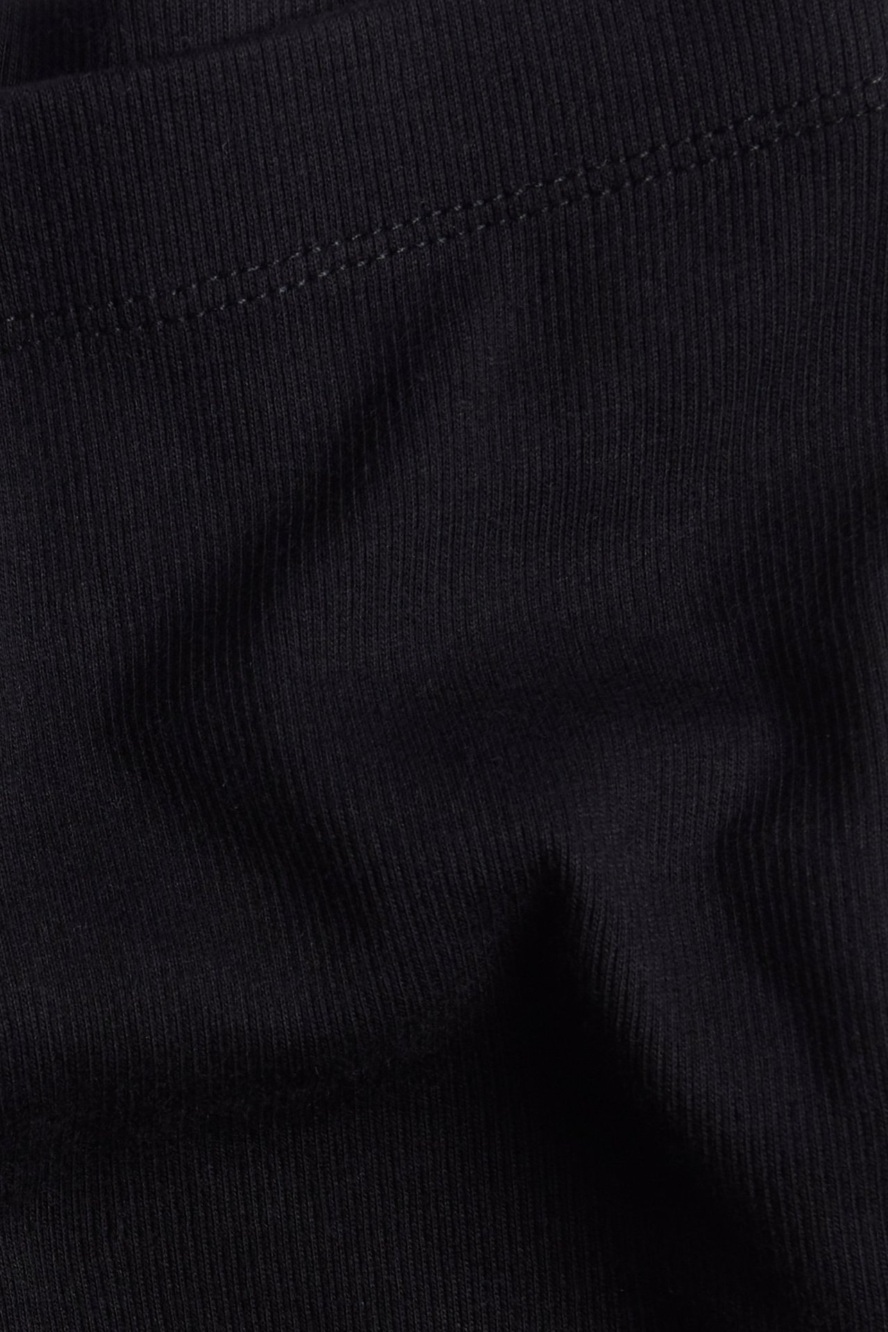 Zbliżenie czarnego, prążkowanego materiału legginsów rowerowych z widocznym szwem.