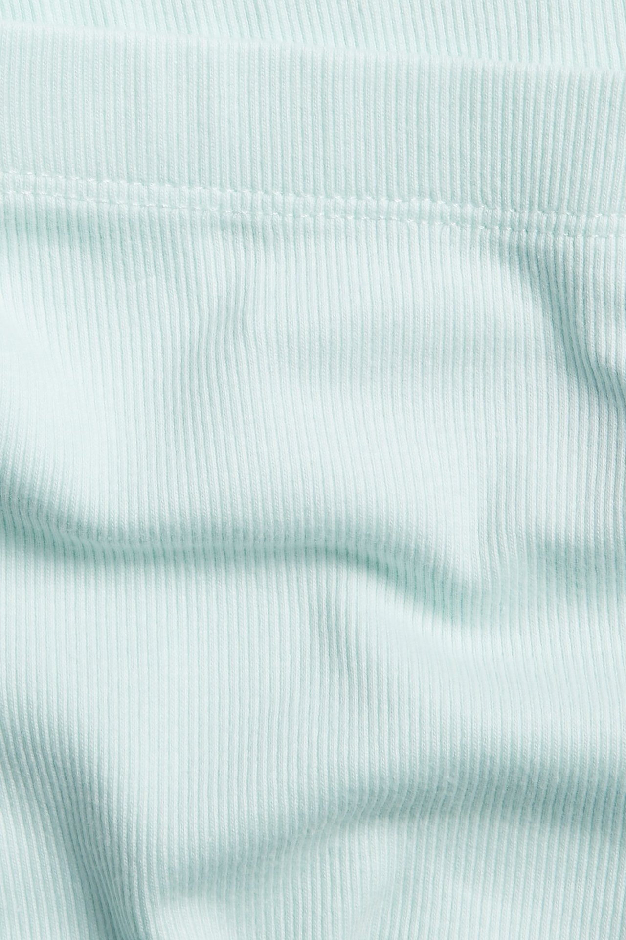 Zbliżenie na jasnozielony, prążkowany materiał legginsów rowerowych, jednolity kolor.