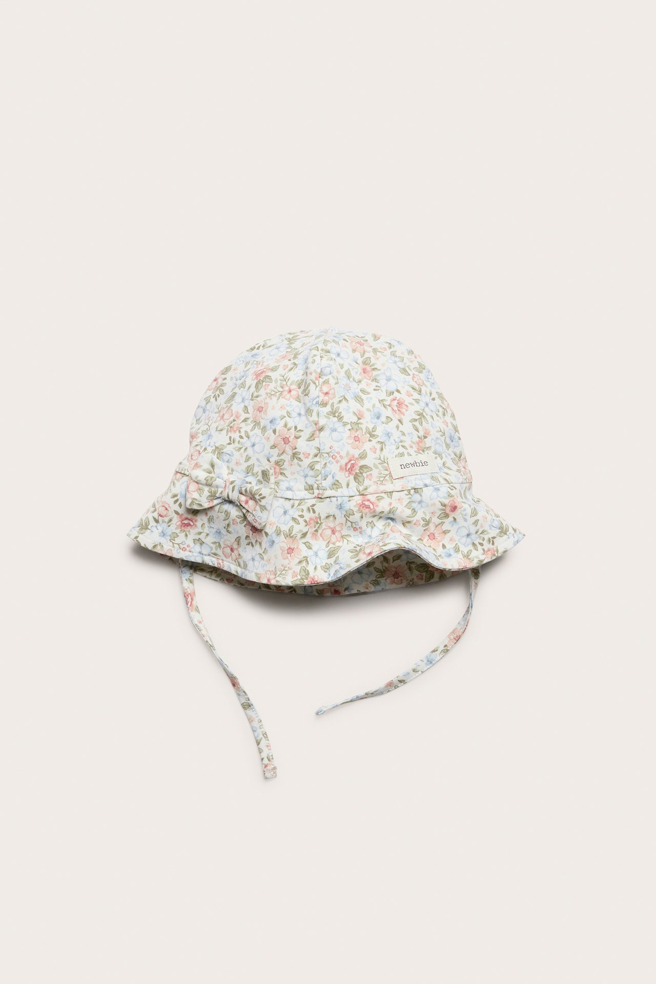 Forfra, offwhite baby solhatt med blomstermønster, sløyfe foran og knytebånd.