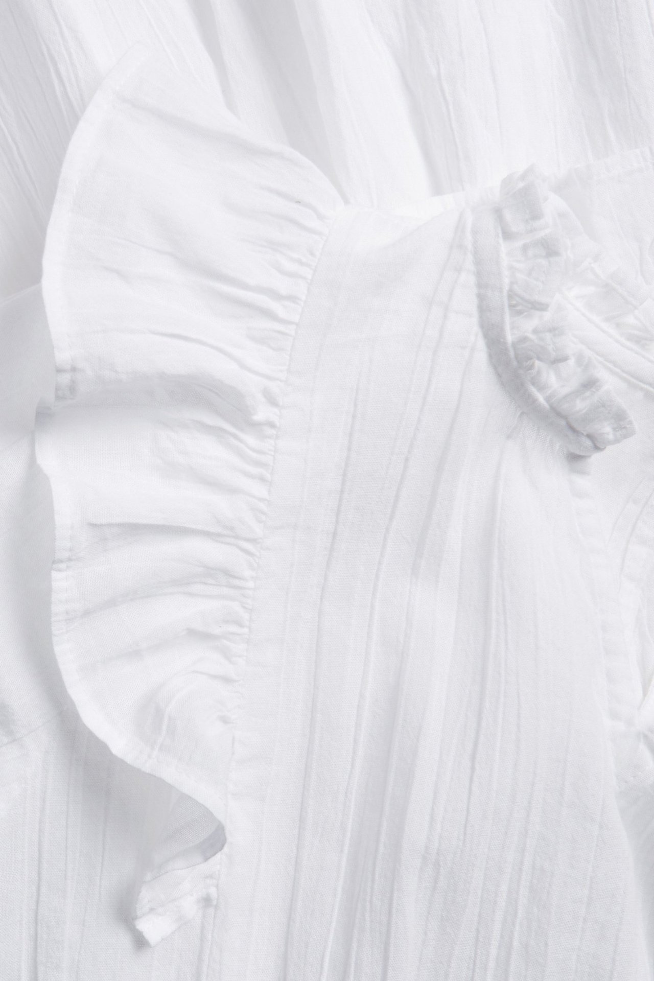Zbliżenie białej, tkanej sukienki dziecięcej z krótkimi falbankowymi rękawami i teksturowanym materiałem.