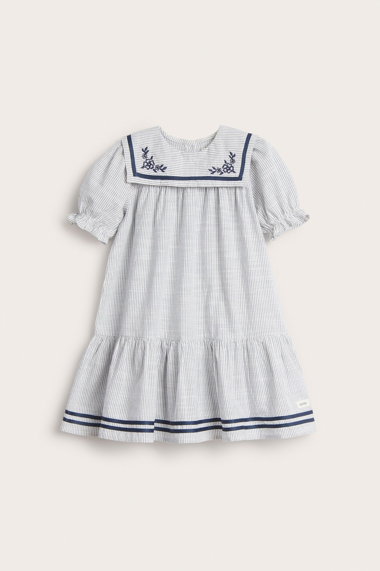 Framsida: Barns off-white randiga bomullsklänning med broderad sjömanskrage, puffärmar och blårandig volangkant.