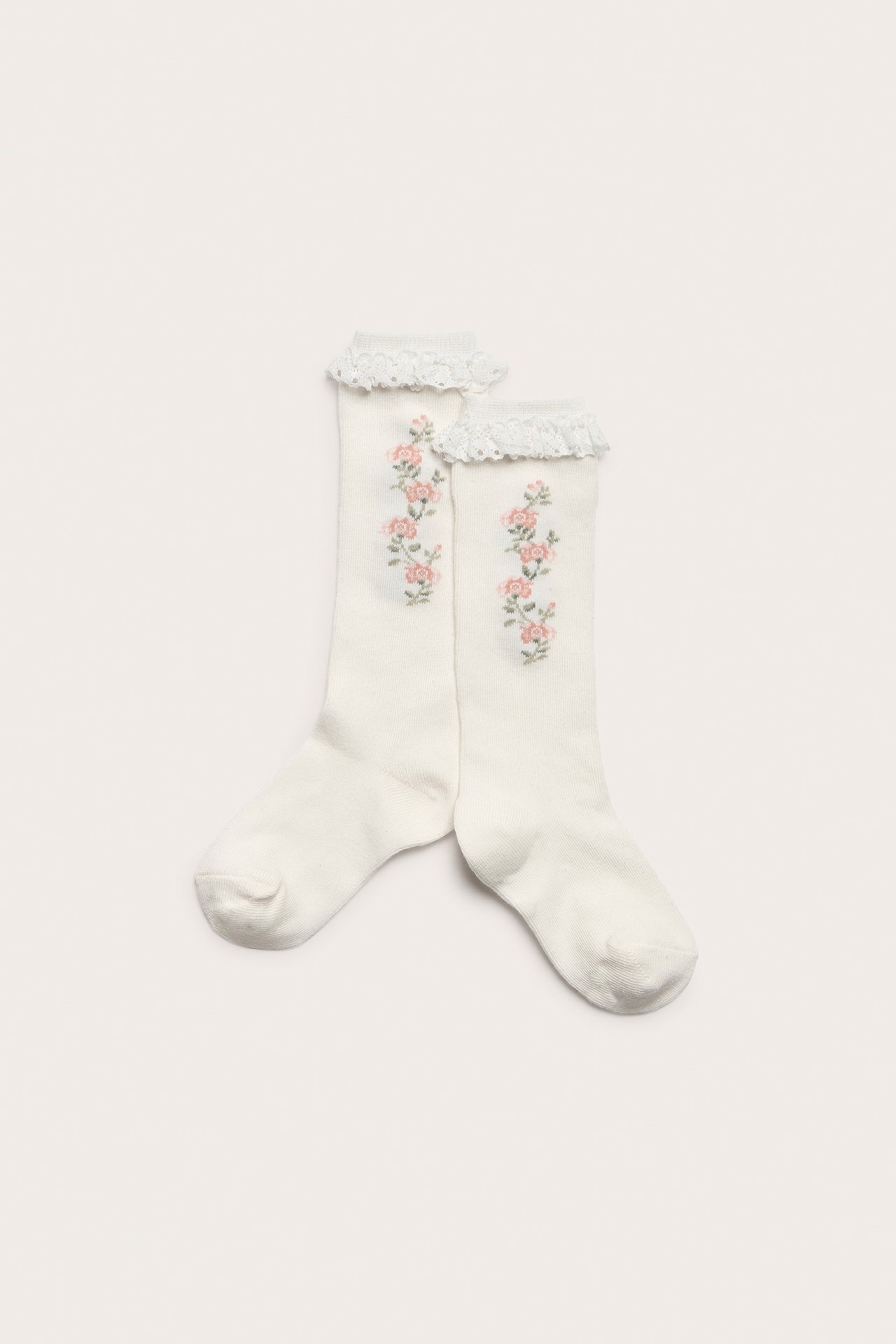 Ovenfra sett par offwhite knestrømper med rosa blomsterbroderi og rysjekant i blonde øverst.
