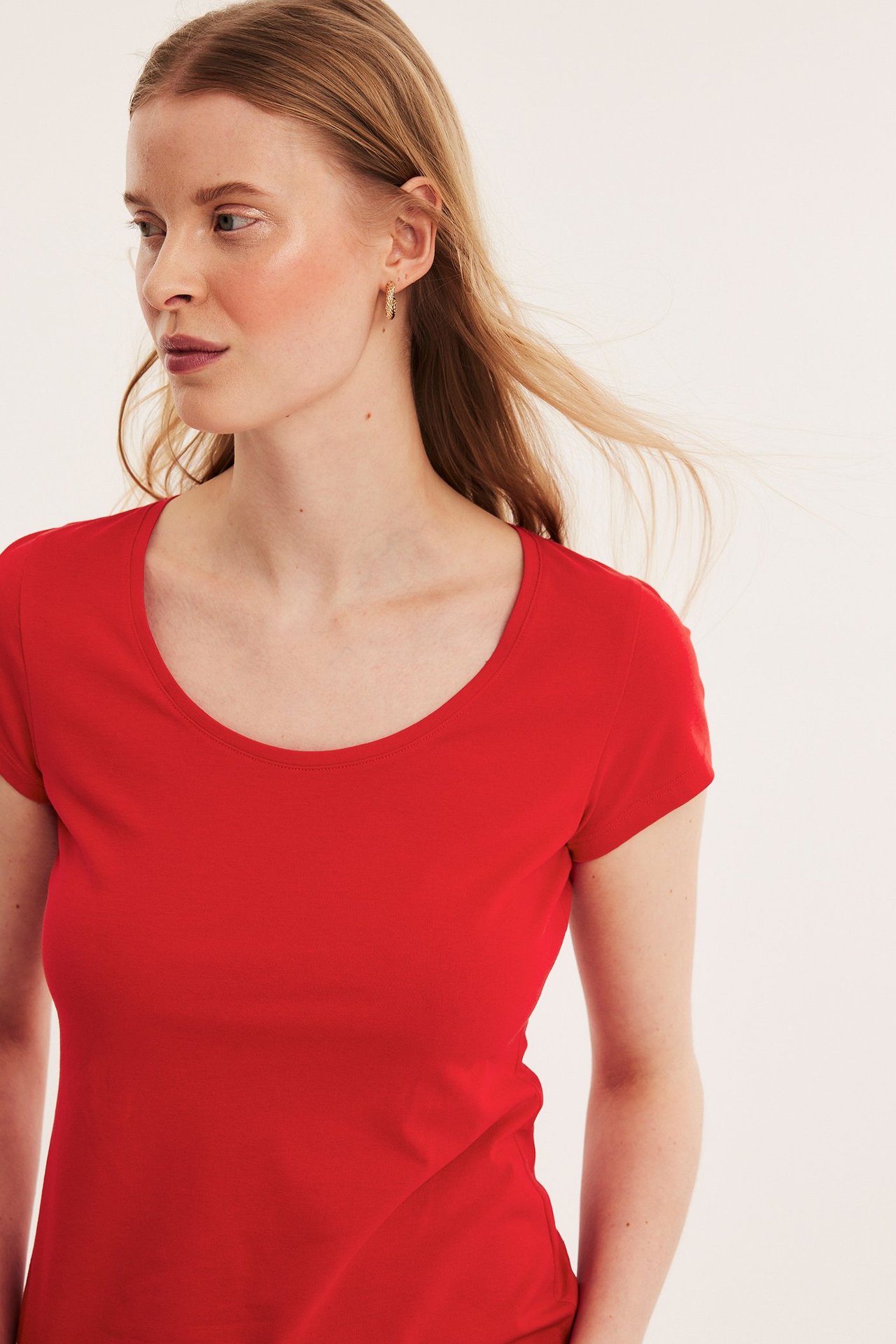 Nærbilde av en kvinne i en rød kortermet bomulls-t-skjorte med scoop-hals og små gulløredobber.