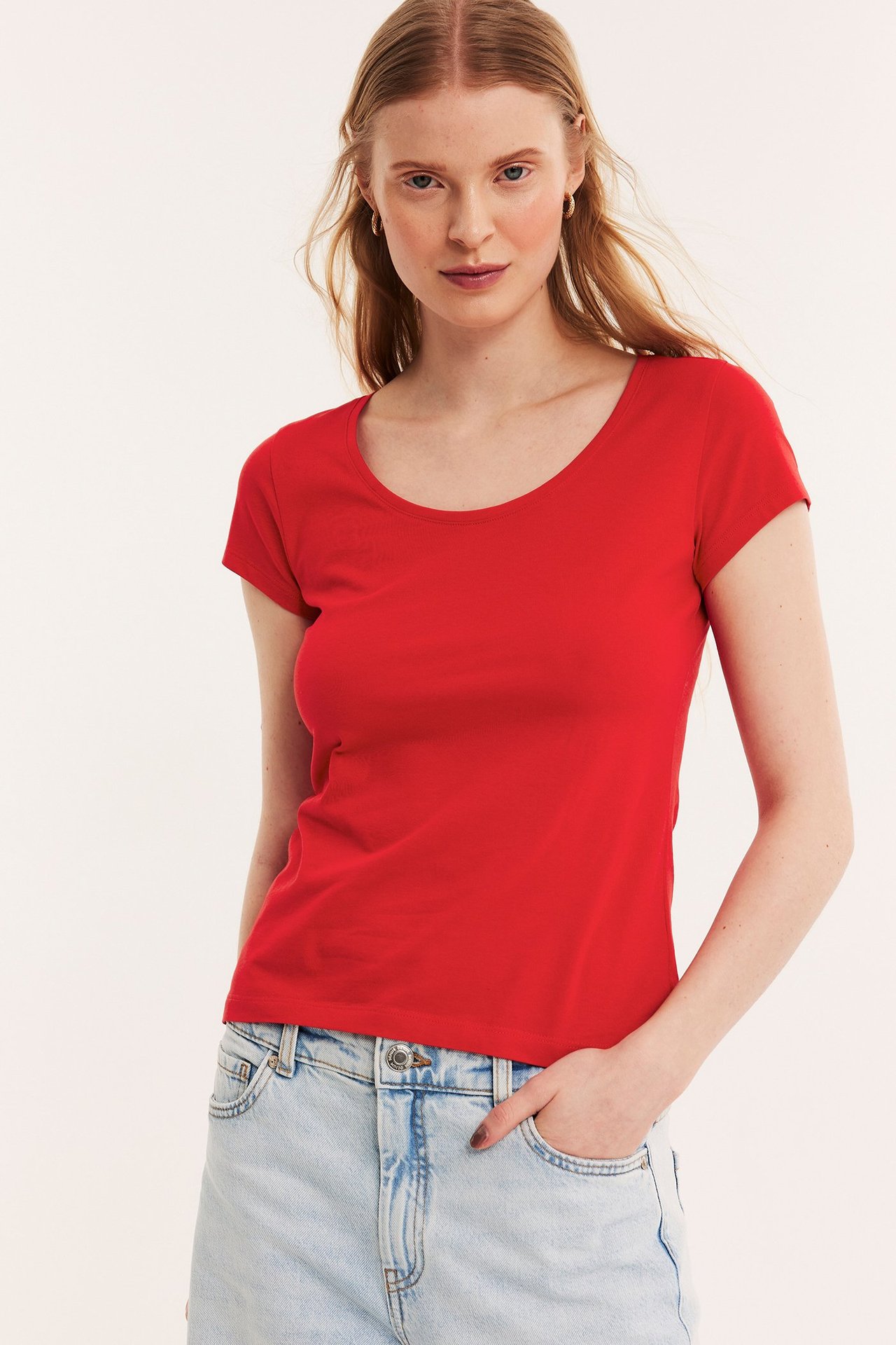 Front: kvinne i rød kortermet bomulls-t-skjorte med scoop-hals og lyseblå jeans.