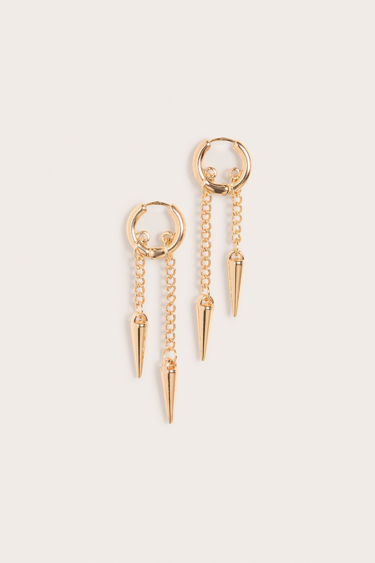 Zbliżenie na dwa złote metalowe kolczyki koła z wiszącymi łańcuszkami i kolczastymi zawieszkami.