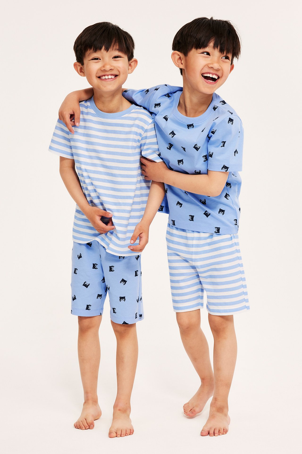 Edestä kaksi lasta vaaleansinisissä puuvillapyjamissa: yksi raidallinen, yksi rapukuvioinen setti.