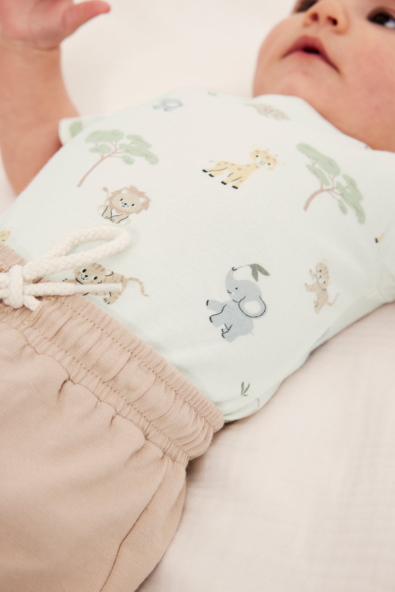 Lähikuva vauvasta yllään luonnonvalkoinen kuviollinen lyhythihainen body ja beiget joustovyötäröiset shortsit.