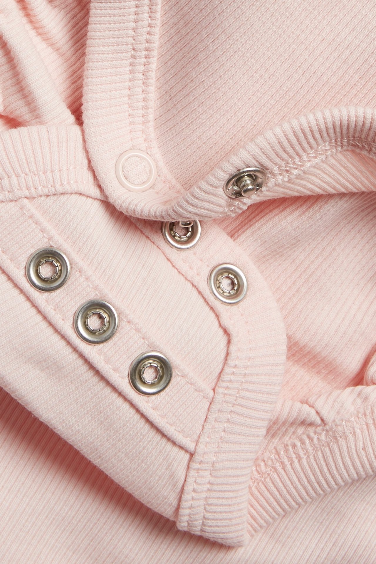 Zbliżenie jasnoróżowego, prążkowanego body niemowlęcego z metalowymi i plastikowymi zatrzaskami.