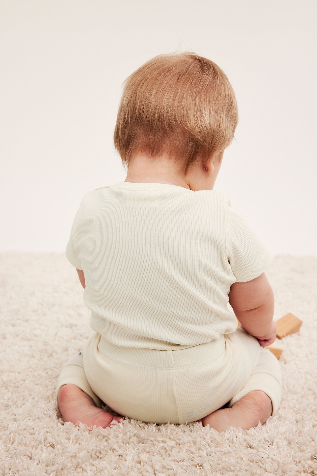 Widok z tyłu na niemowlę w jasnobeżowym prążkowanym body z krótkim rękawem i pasujących spodniach.