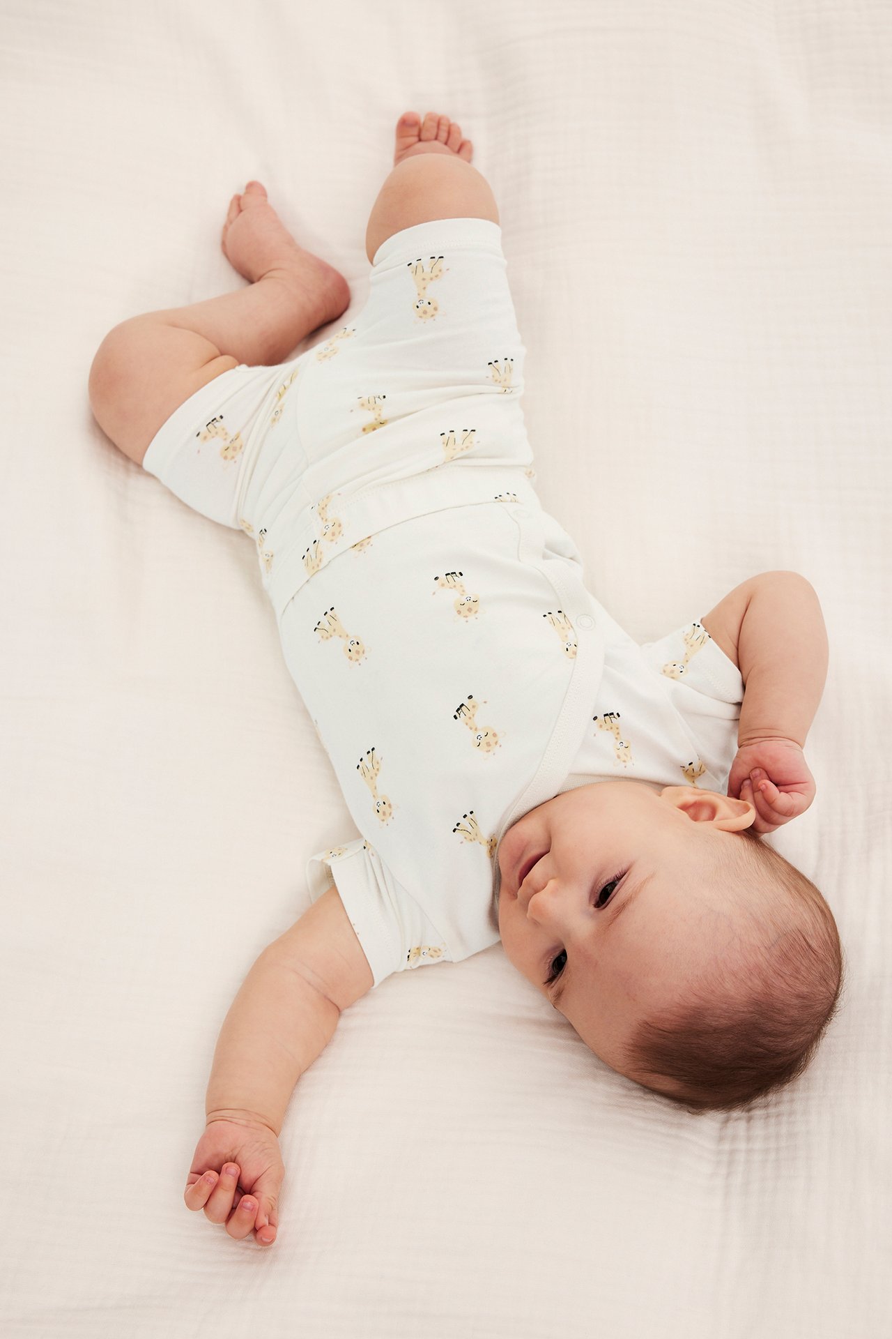 Uppifrån-vy av en baby i offwhite cykelbyxor med giraffmönster och matchande kortärmad topp.