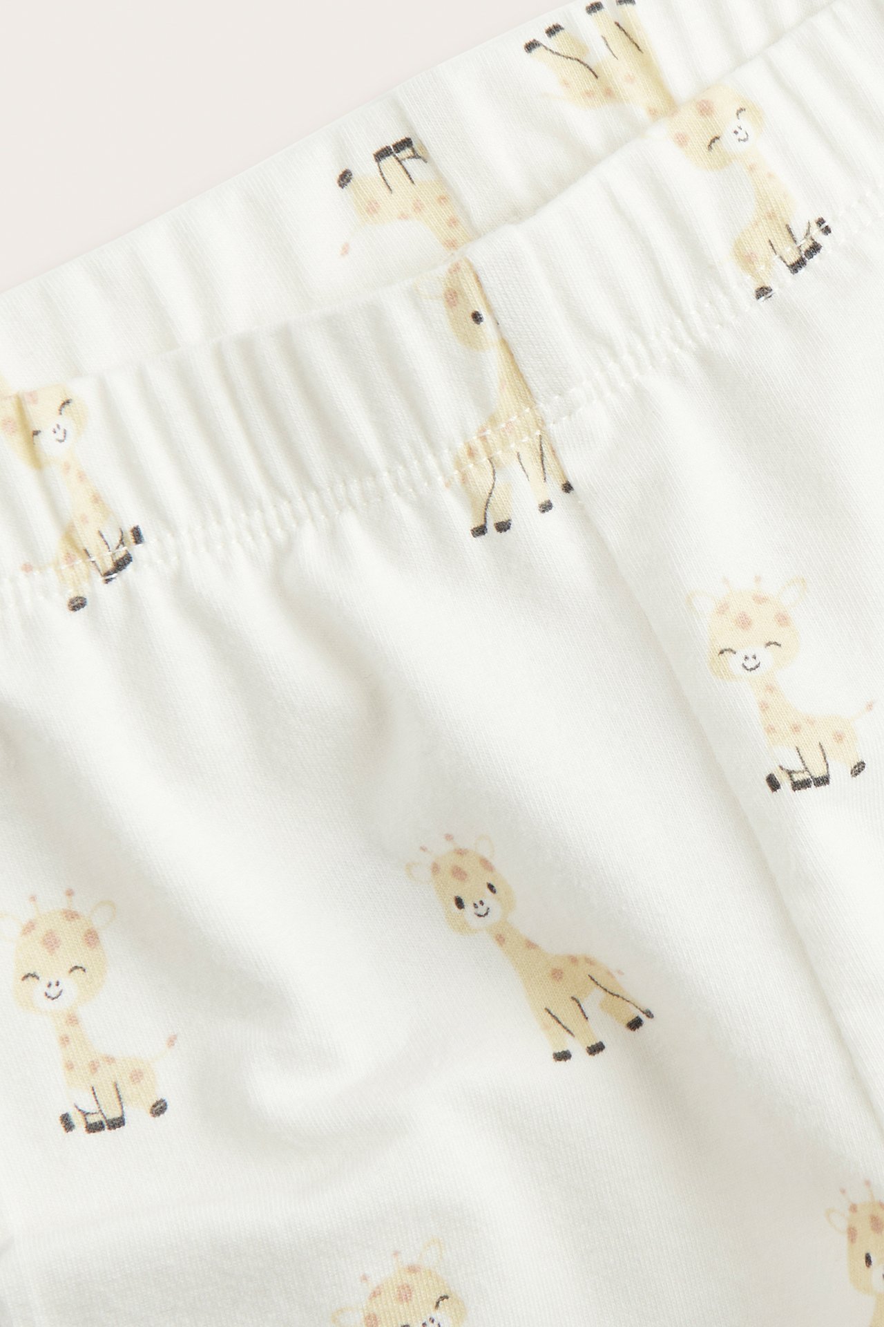 Närbild av offwhite babycykelbyxor med heltäckande giraffmönster och mjuk resår i midjan.