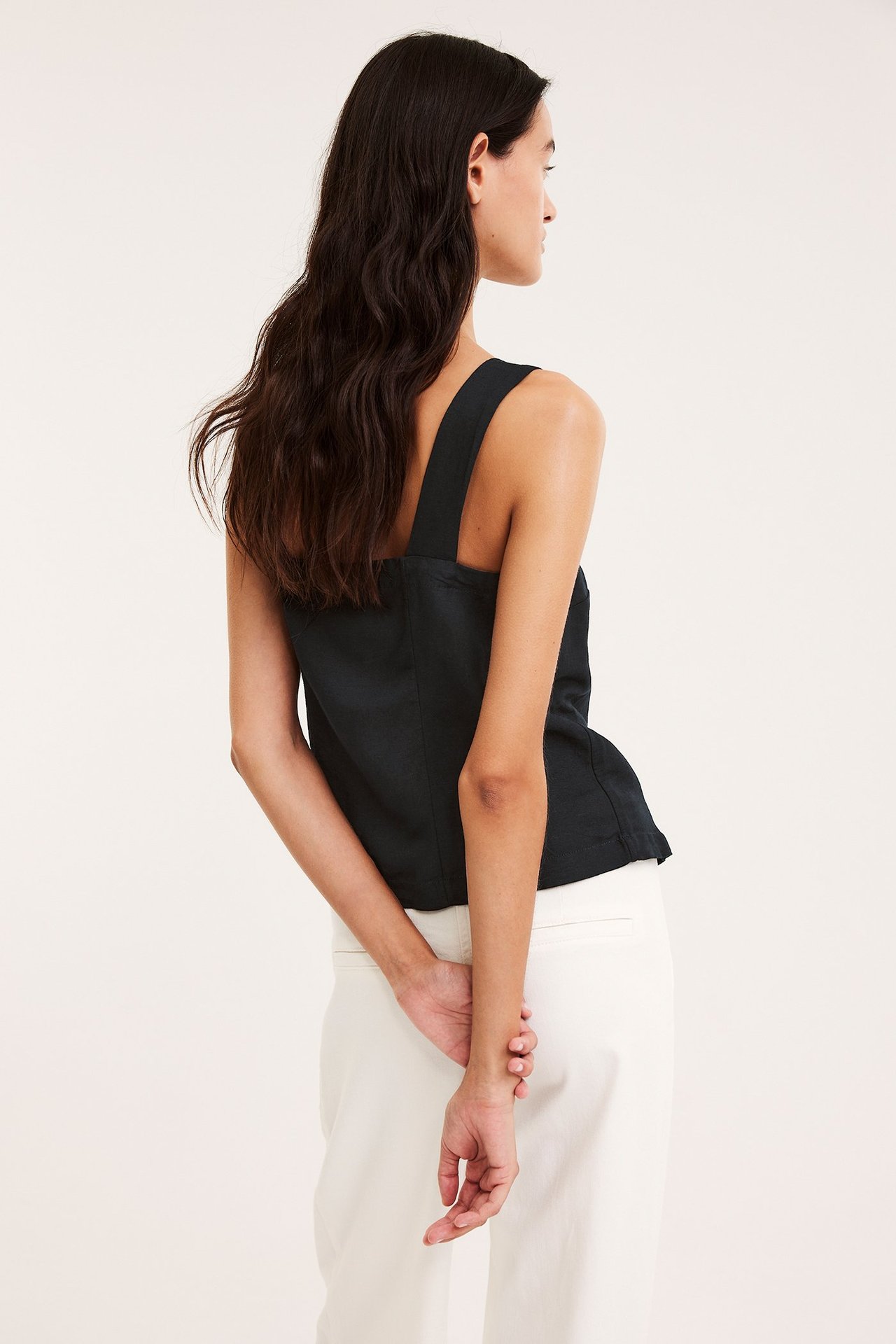 Rygg- och sidovy av en kvinna i svart linneblandningslinne och vita byxor.