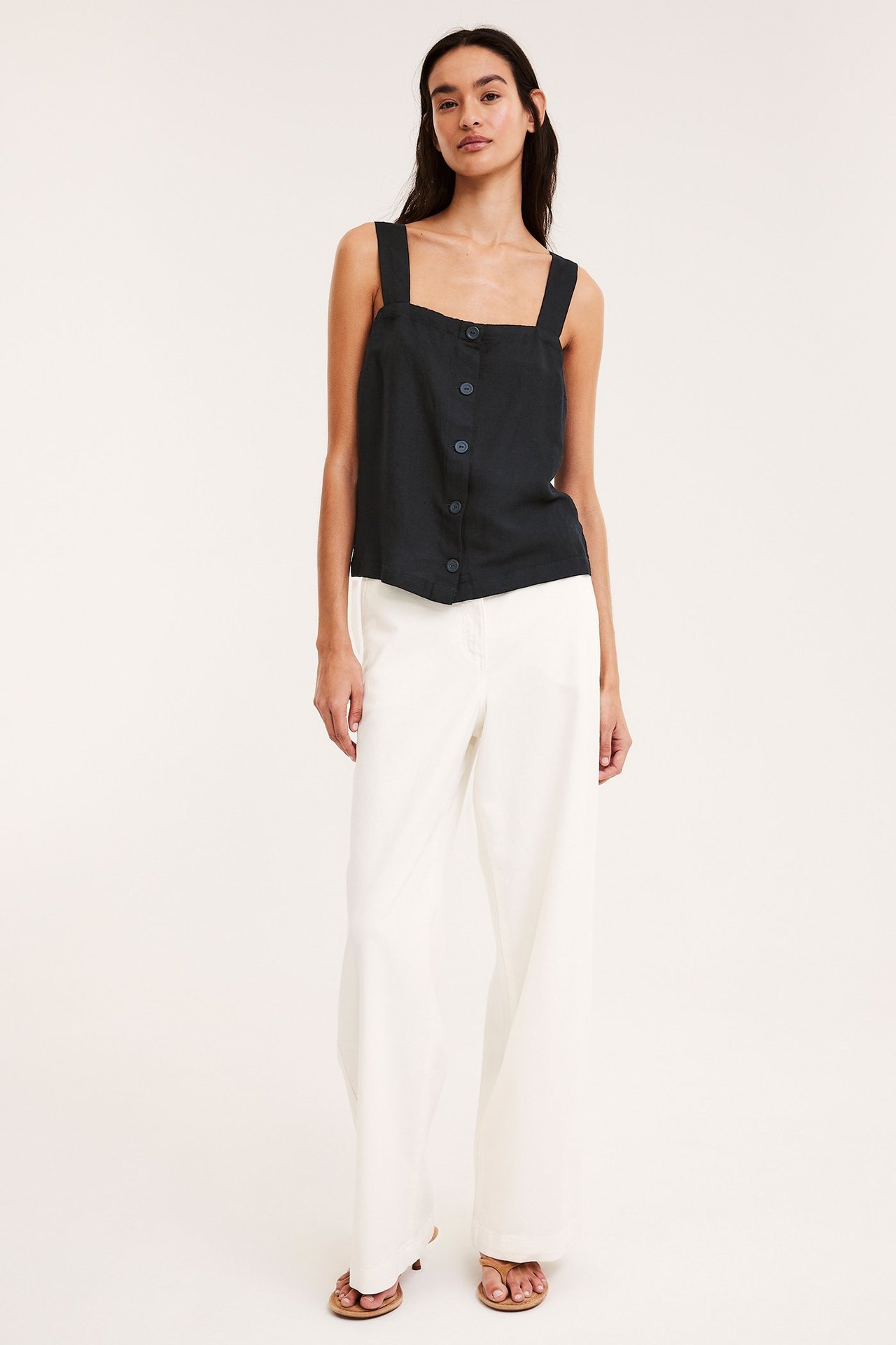 Front view: Kvinna i svart linnemix-linne med knappar fram och vita vida byxor.