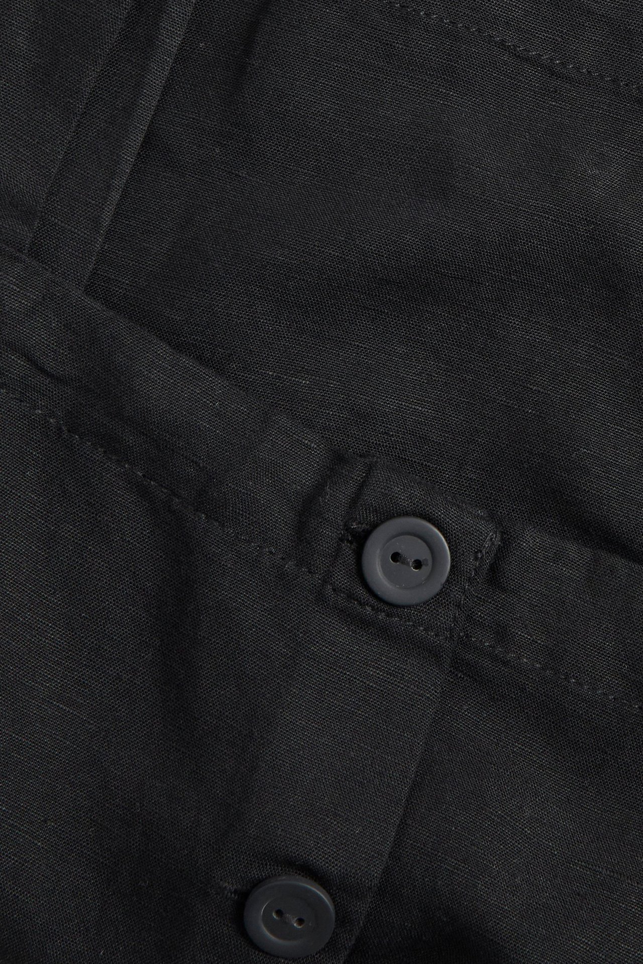 Zbliżenie czarnego topu z mieszanki lnu z dwoma ciemnoszarymi guzikami.