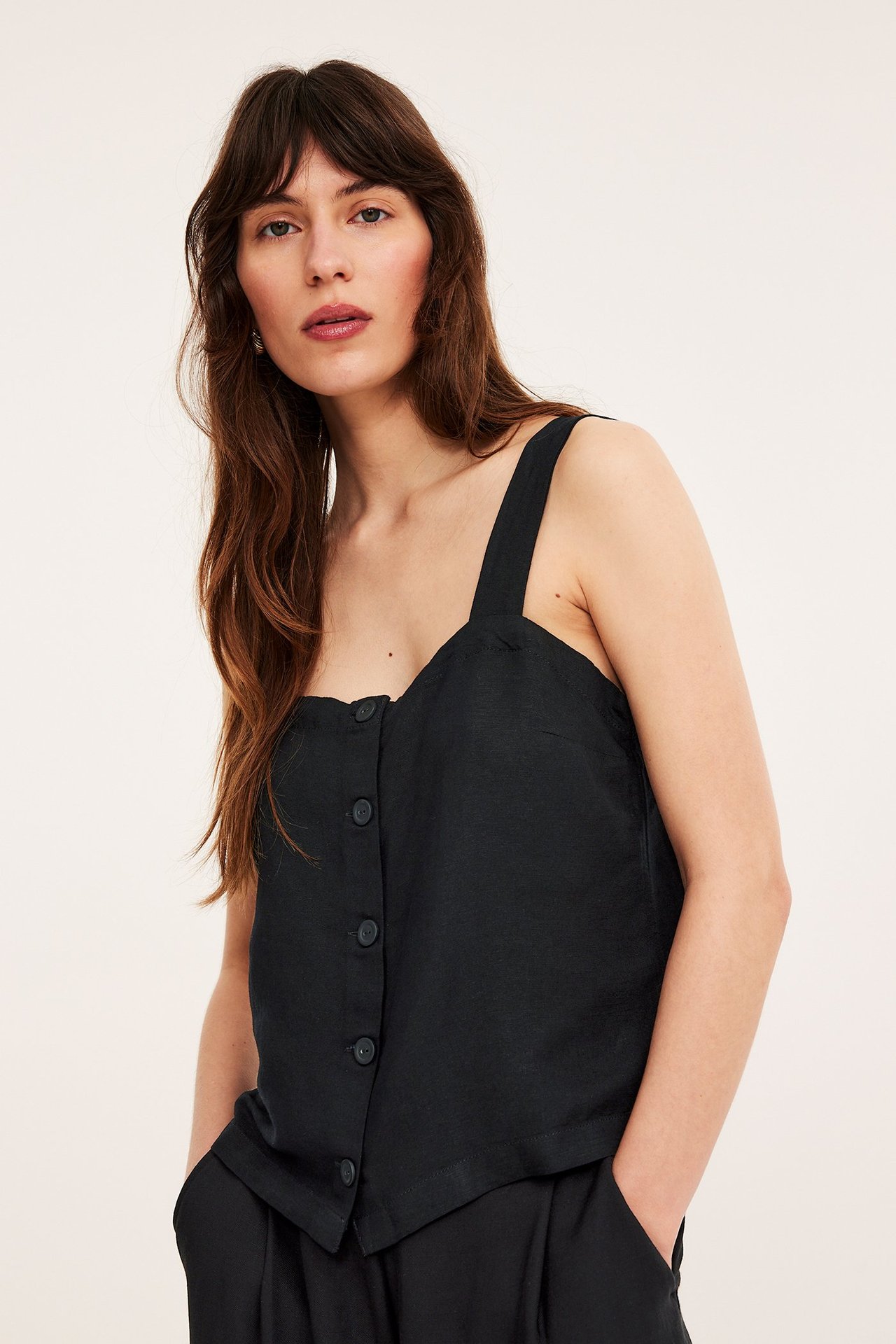 Frontbilde av en kvinne i svart linblandingstopp med knapper og svarte bukser.