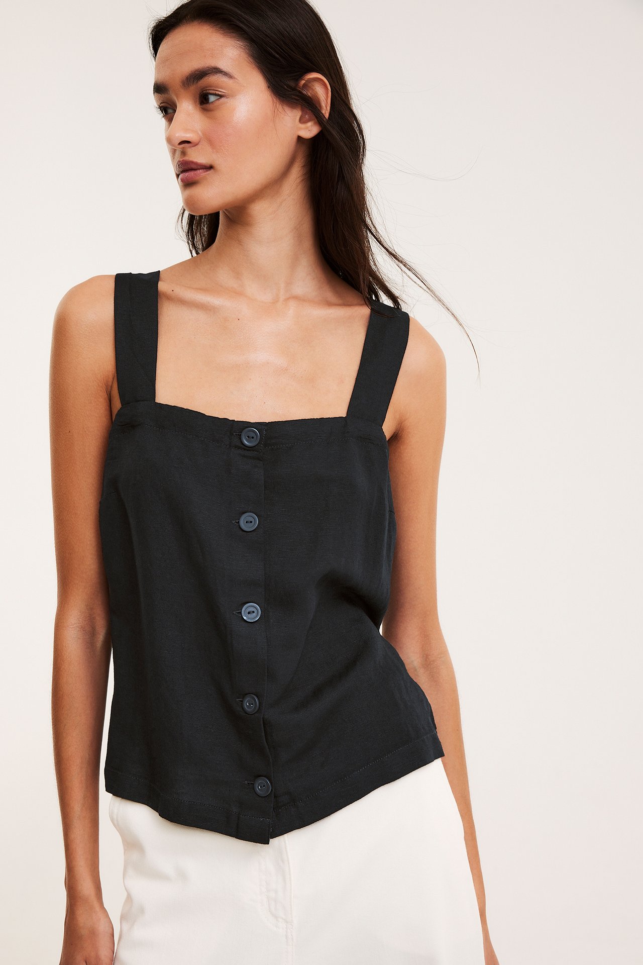 Naisen etunäkymä: musta pellavasekoitetoppi edessä napeilla, yhdistettynä valkoisiin housuihin.